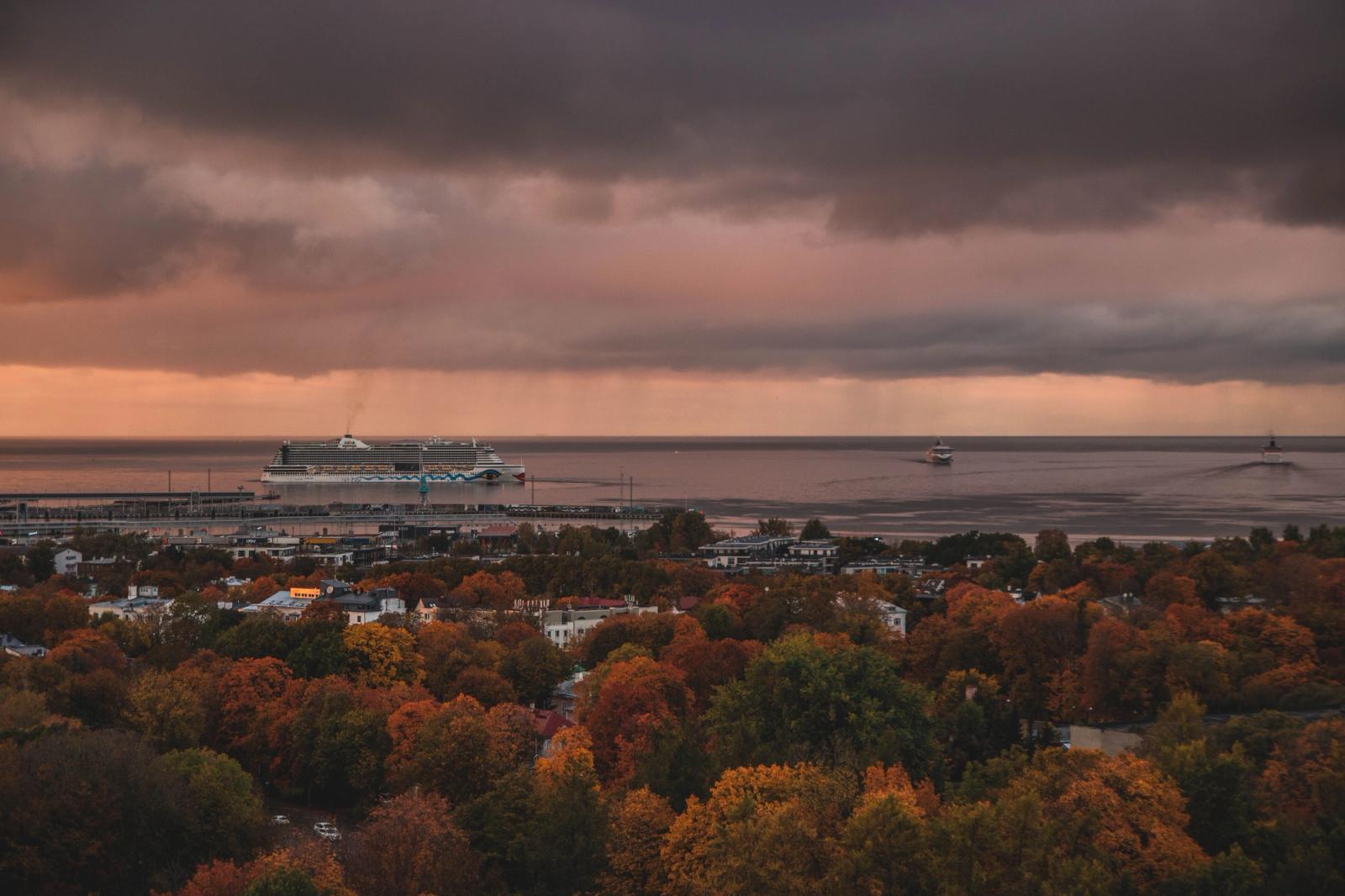 A captivating view of a harbor at sunset in autumn, showcasing a cruise ship on the horizon under dramatic clouds