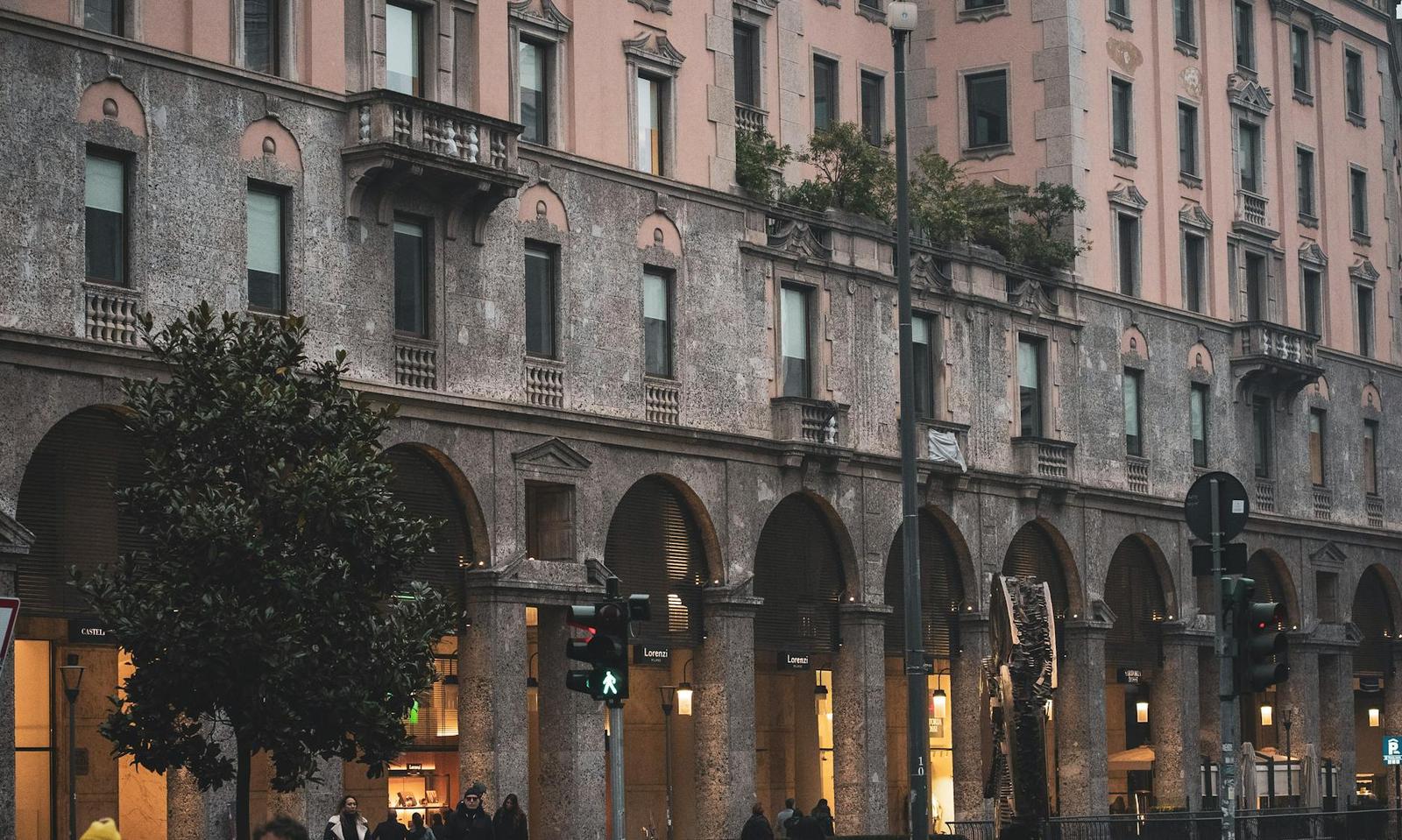 Arcaded stone street facade with pedestrians walking beneath the columns