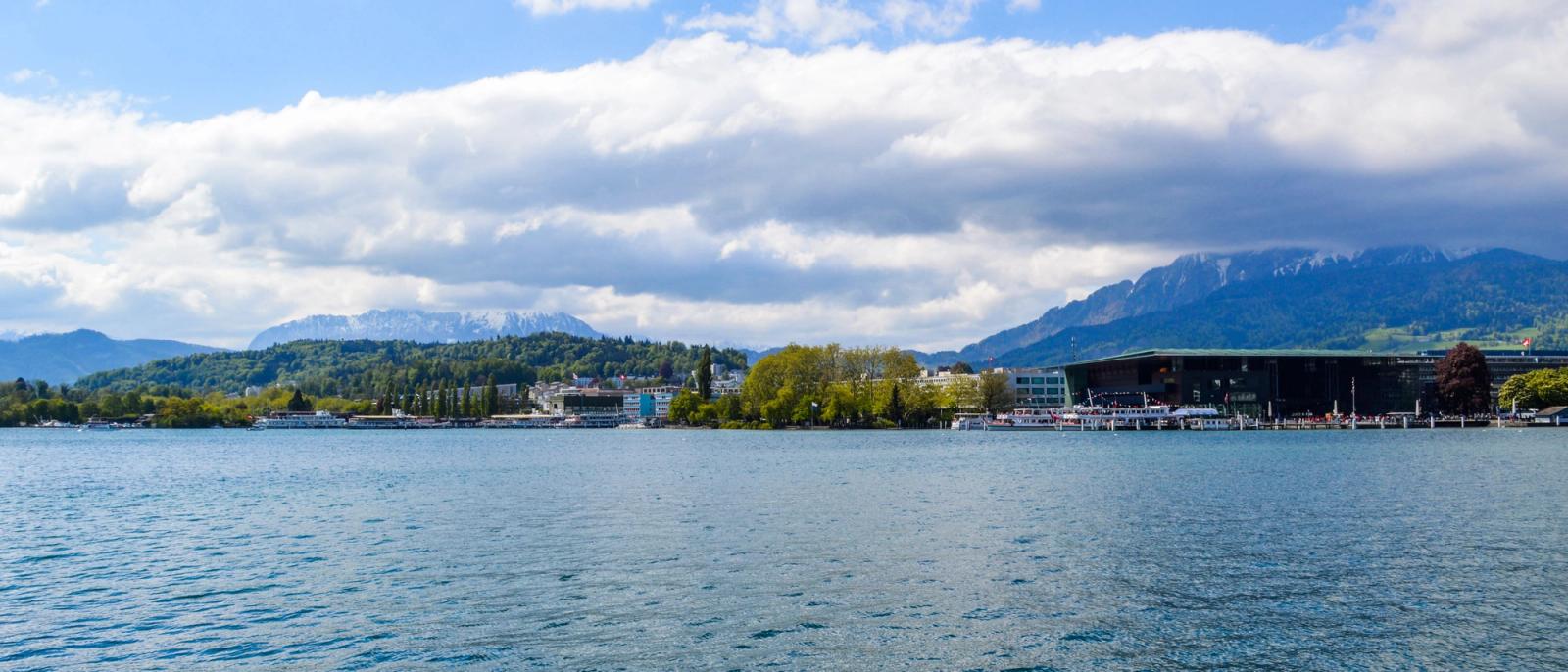 Panoramic view of tranquil lake water with dock building and greenery on coast under clouds