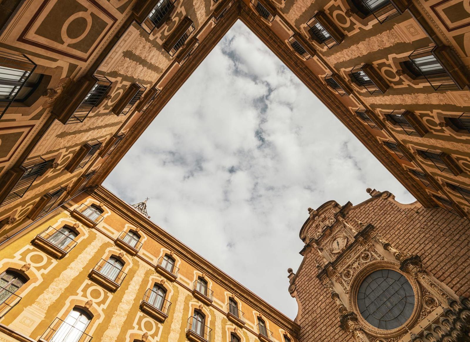 Looking up between ornate stone buildings to a triangular patch of sky and a church dome