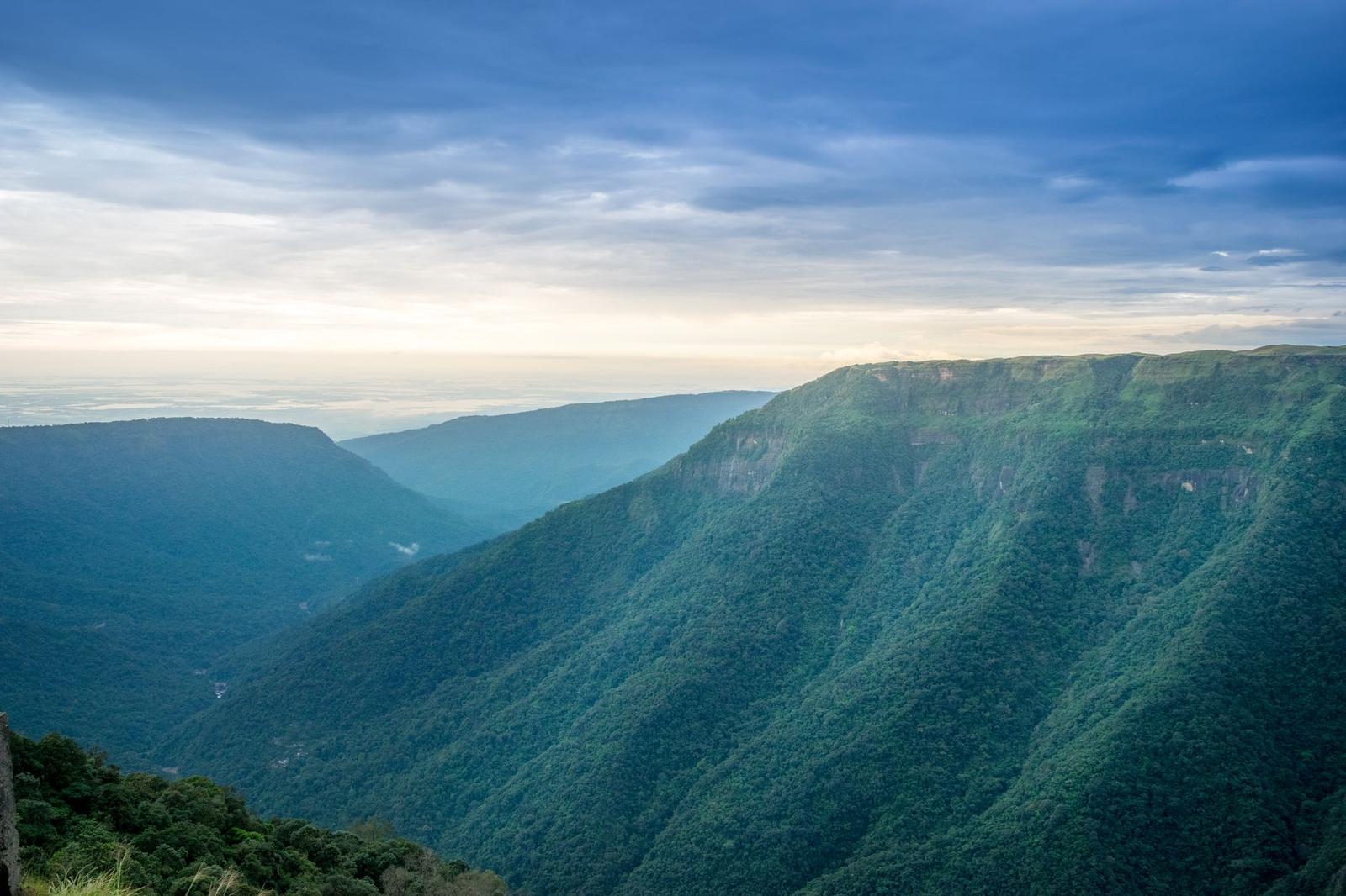 A deep forested gorge with layered ridgelines fading into hazy distance under clouds