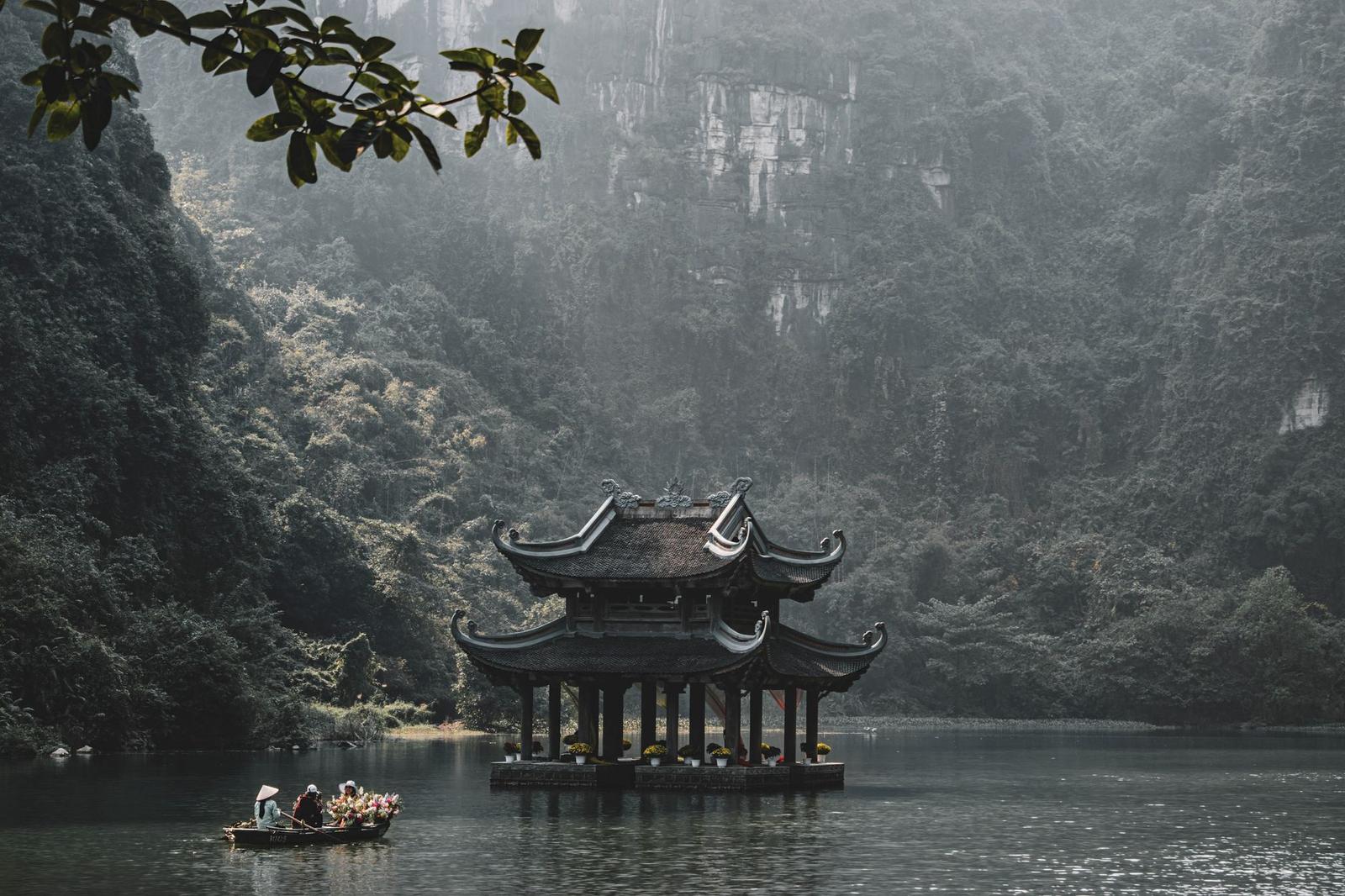 Serene scene of a traditional pagoda on the Tam Coc river in Ninh Bình, surrounded by lush greenery