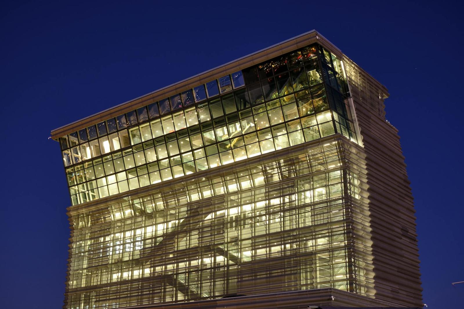 A glass-walled building glows against a deep blue evening sky