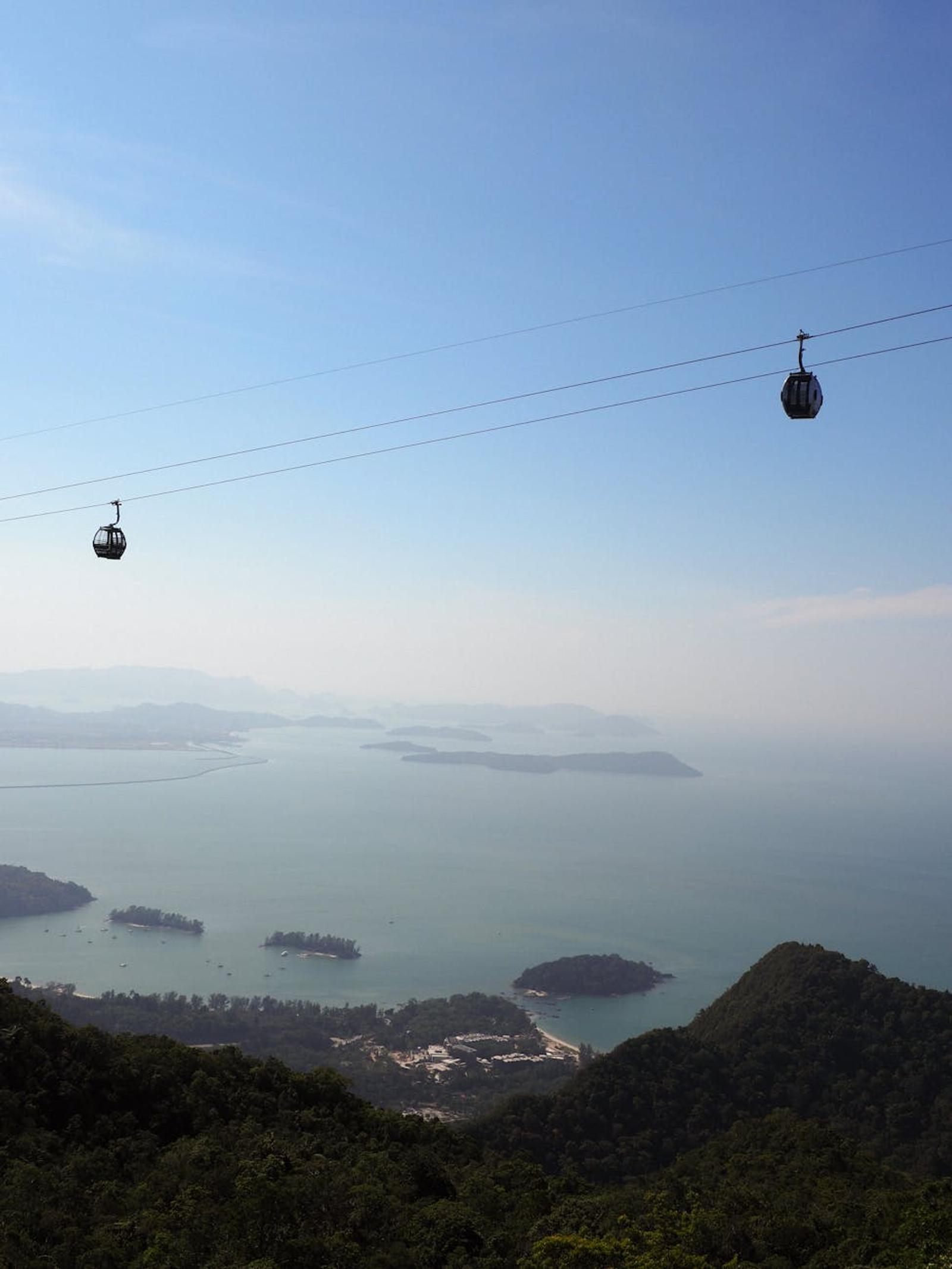 Cable cars descending a forested hillside toward a hazy island-dotted sea