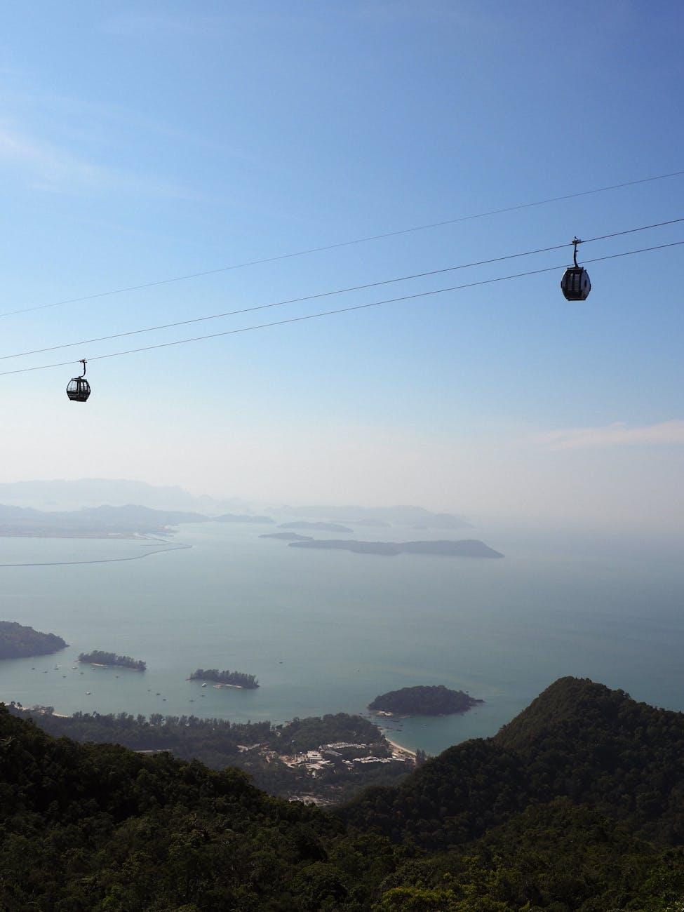Cable cars descending a forested hillside toward a hazy island-dotted sea