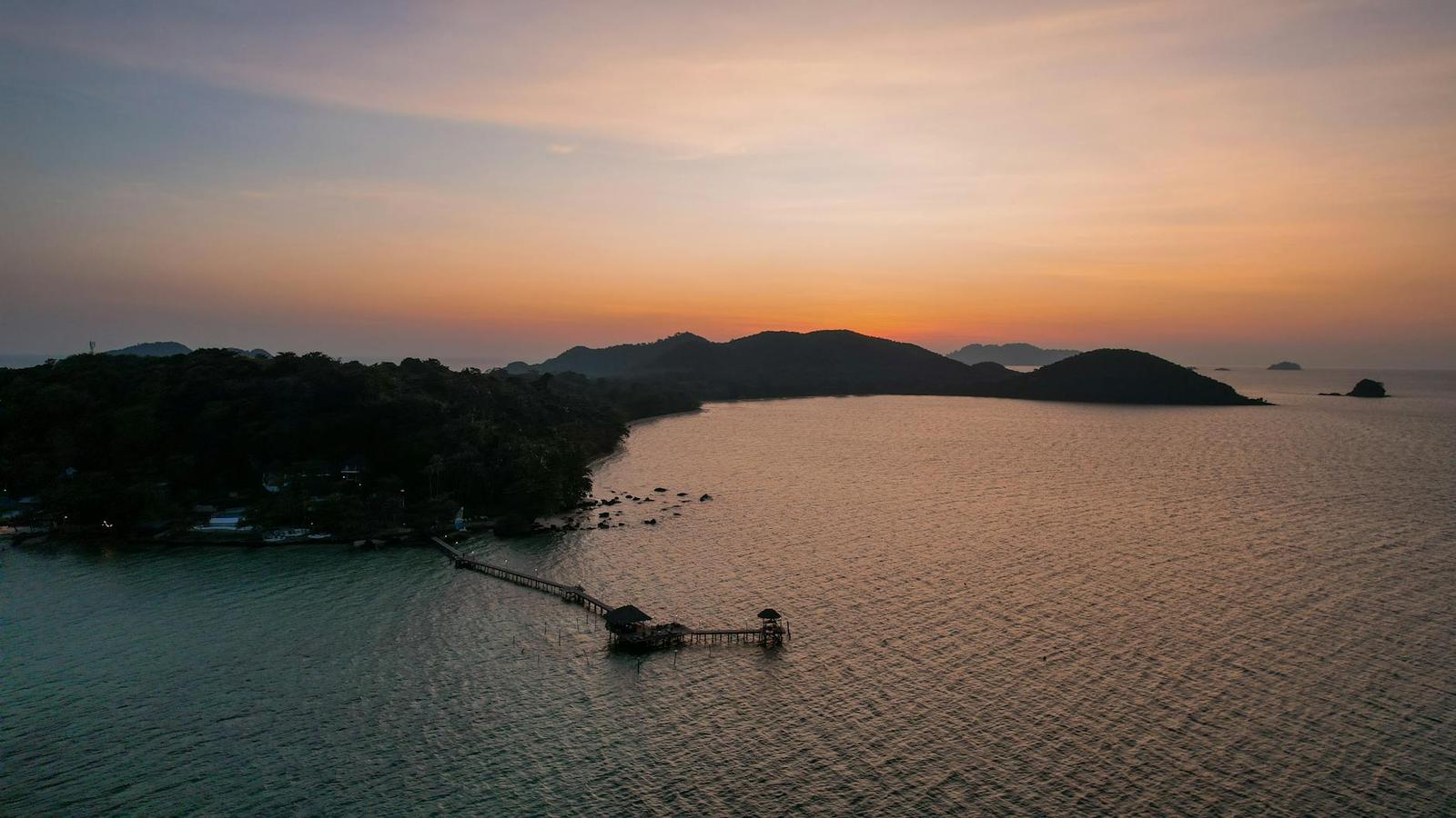 Aerial view of a wooden pier reaching into calm water at dusk