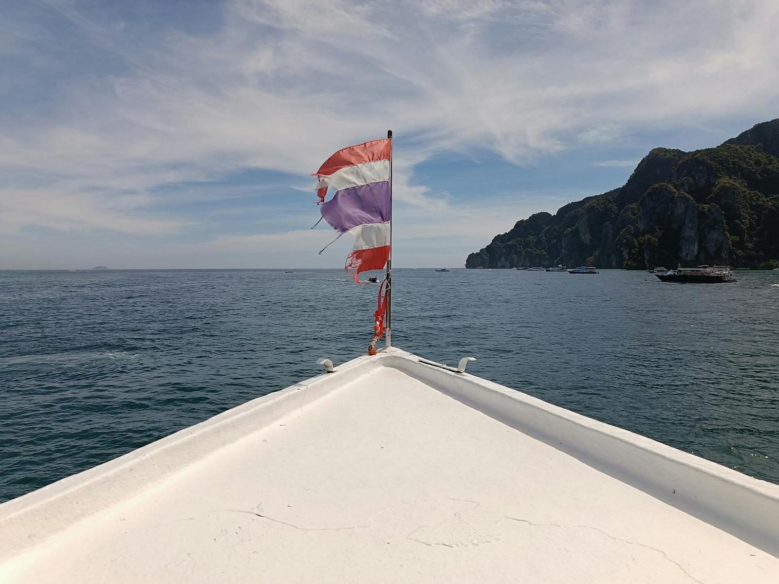 A boat's bow with fluttering flags heading toward distant limestone cliffs