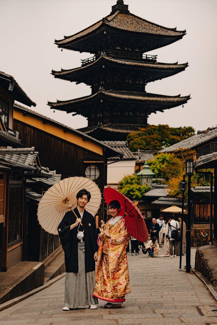 Couple in traditional kimono holding paper umbrellas on a lane before a wooden pagoda