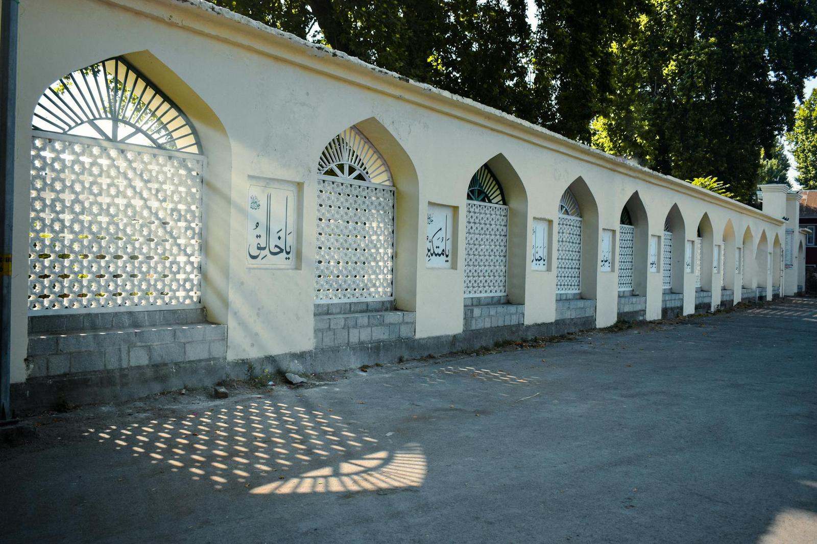 A row of arched calligraphy-carved niches along a sunlit courtyard wall