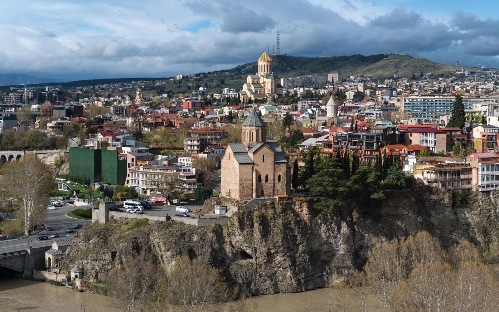 A panoramic view of Tbilisi, Georgia featuring historic churches and diverse architecture under a dramatic sky
