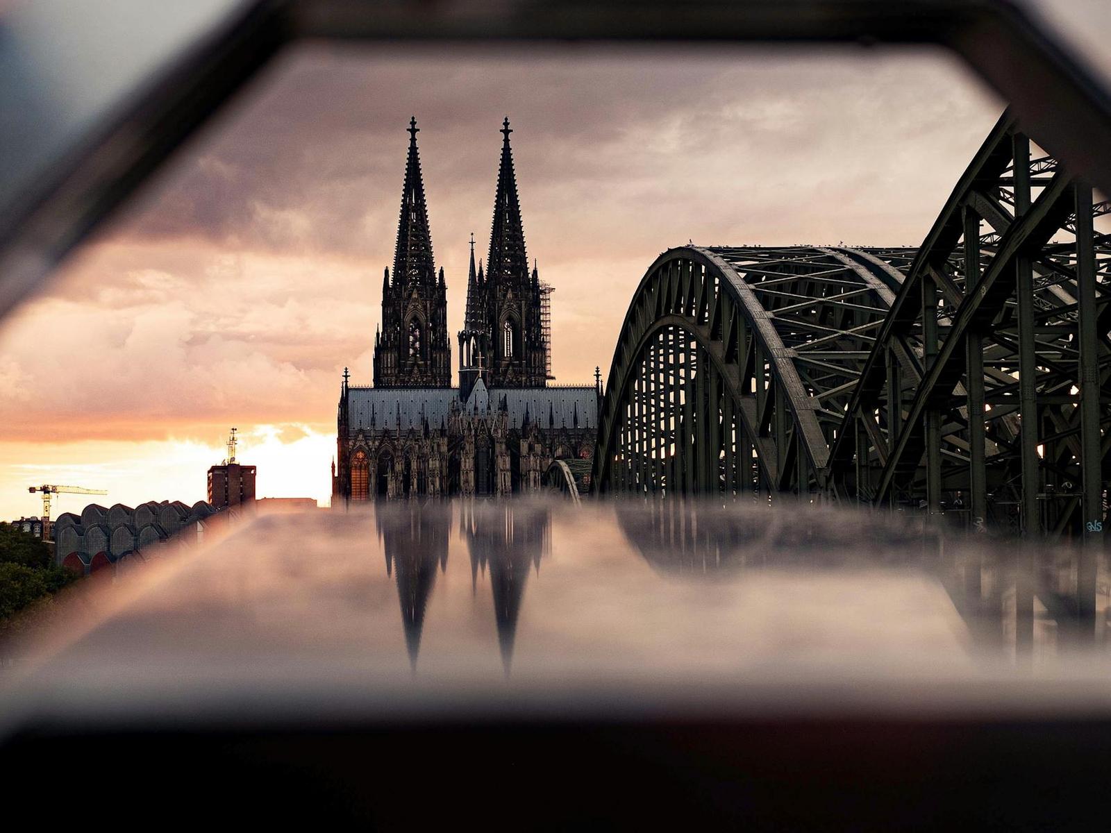 Twin-spired gothic cathedral framed by a steel railway bridge at sunset