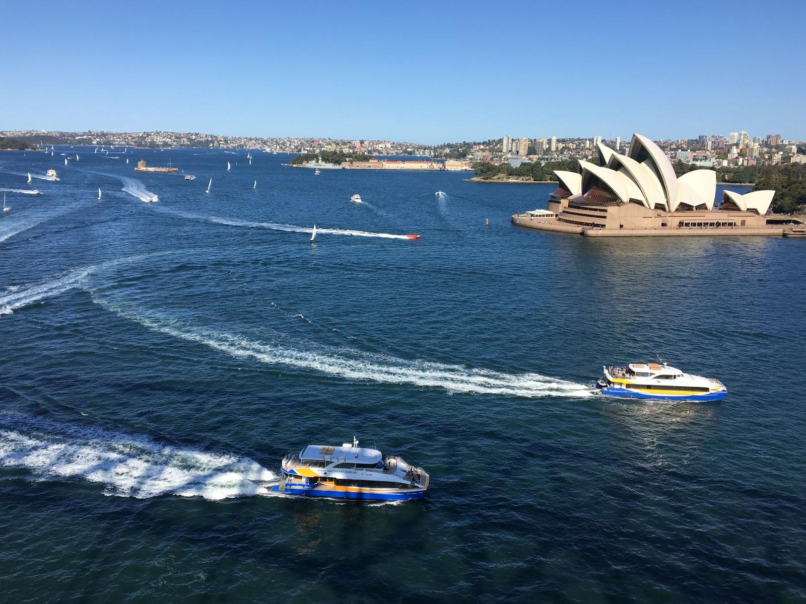 Aerial view of Sydney Harbour featuring the Opera House and ferries under a clear blue sky