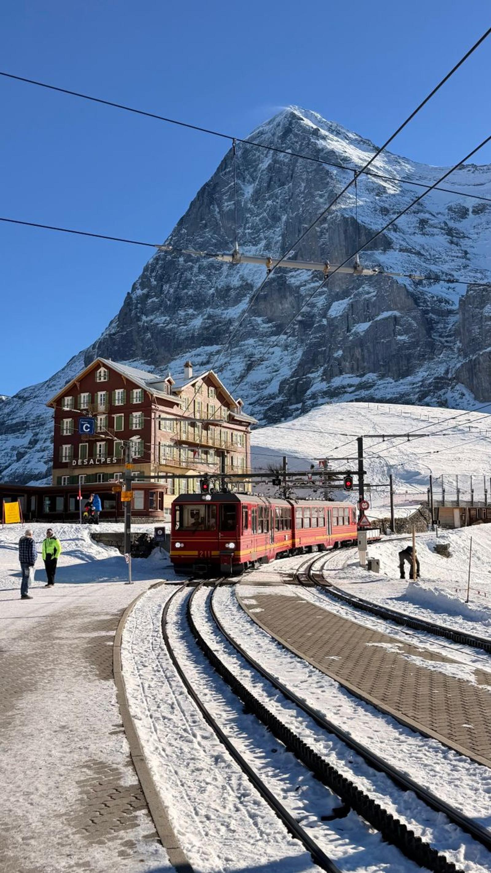 Red mountain train at a snowy station beneath a towering rock face