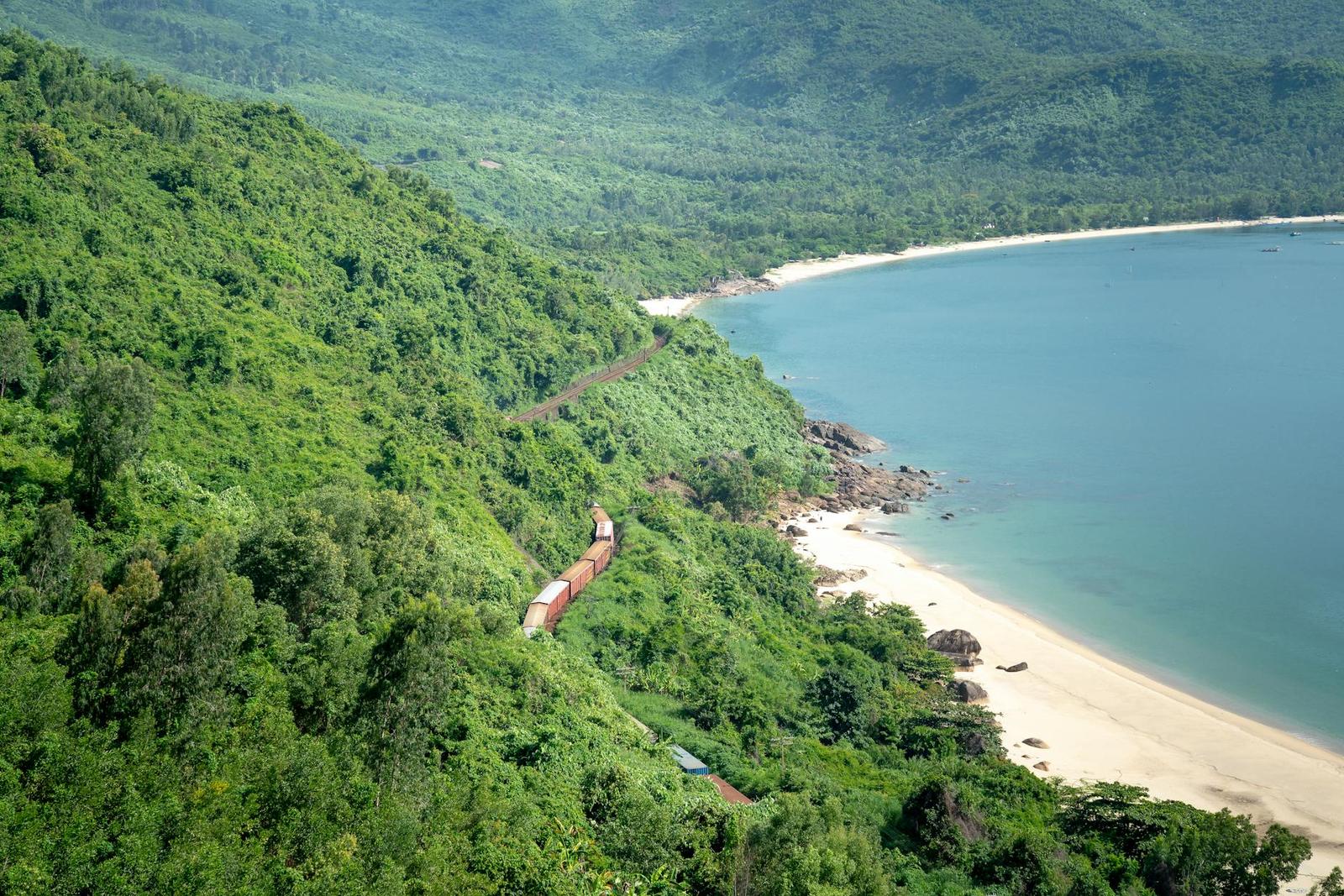Aerial view of a forested coastal pass winding above a sandy bay