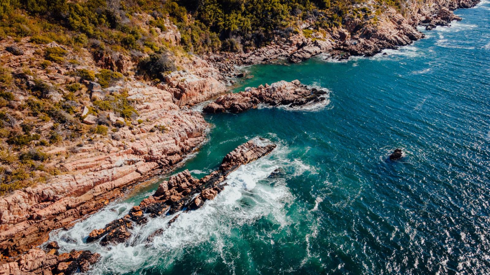 Breathtaking aerial shot of Cape Town's rugged coastal cliffs meeting the vibrant ocean waves
