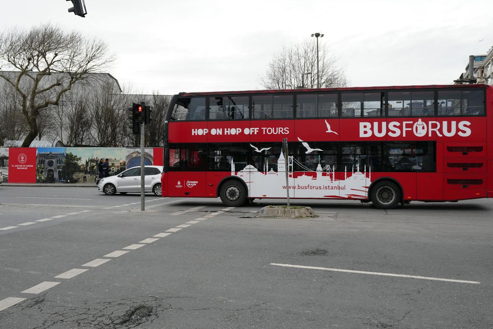A red double-decker tour bus in İstanbul, featuring iconic city landmarks on its side