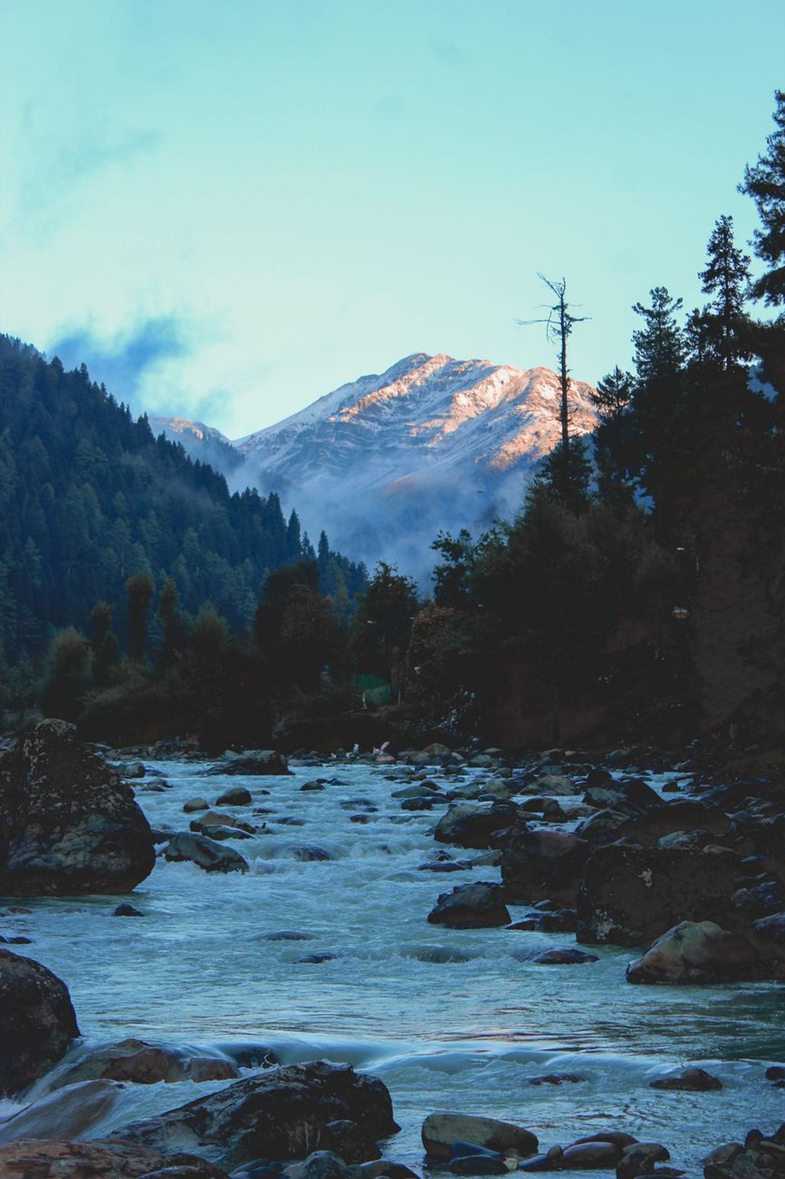 Serene river flowing through rocky landscape with mountain backdrop in Pahalgam