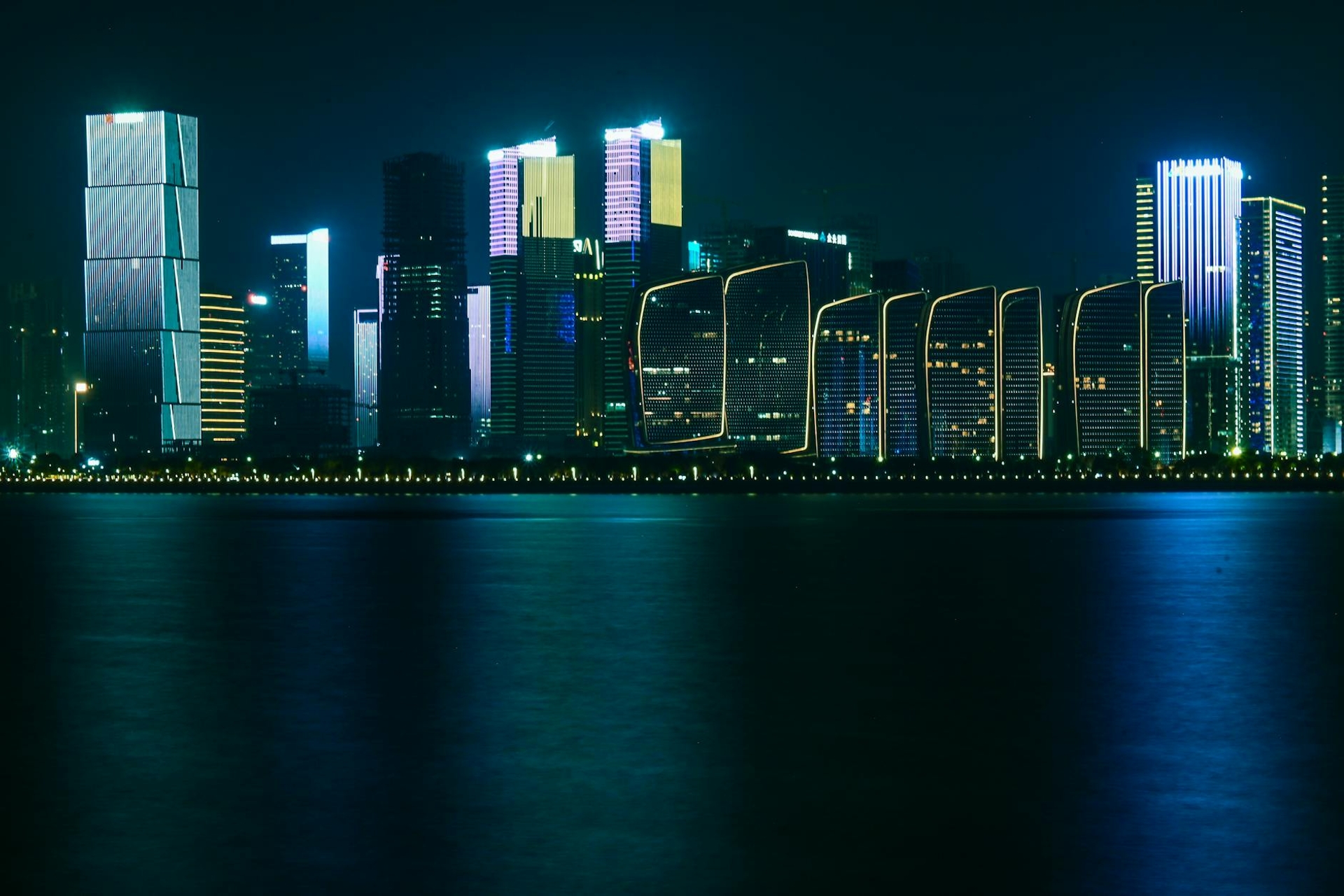 A neon-outlined city skyline glowing above dark water at night