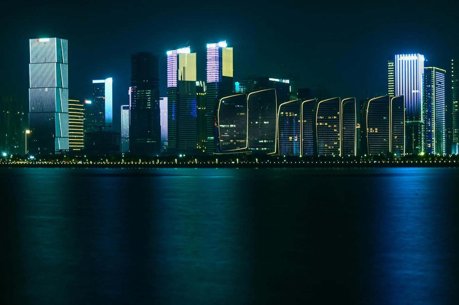A neon-outlined city skyline glowing above dark water at night