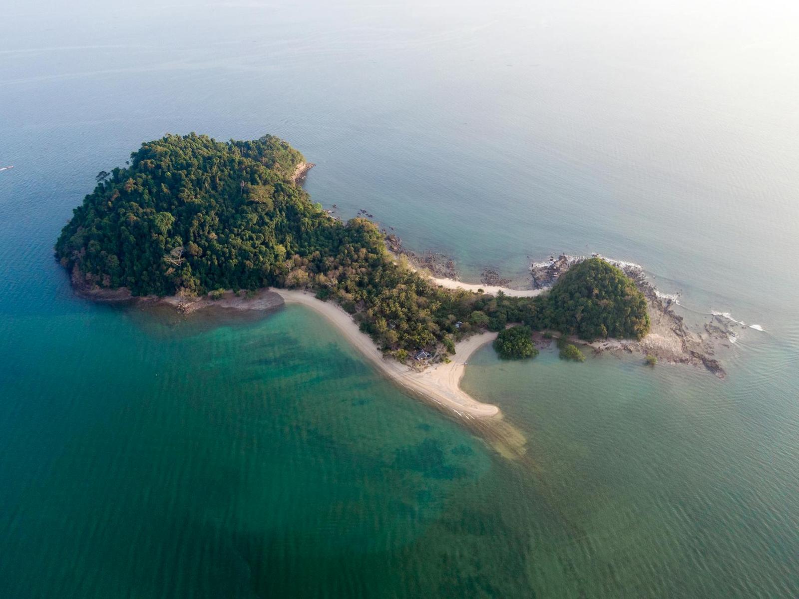 Aerial view of a forested island with a narrow sandy isthmus meeting turquoise water