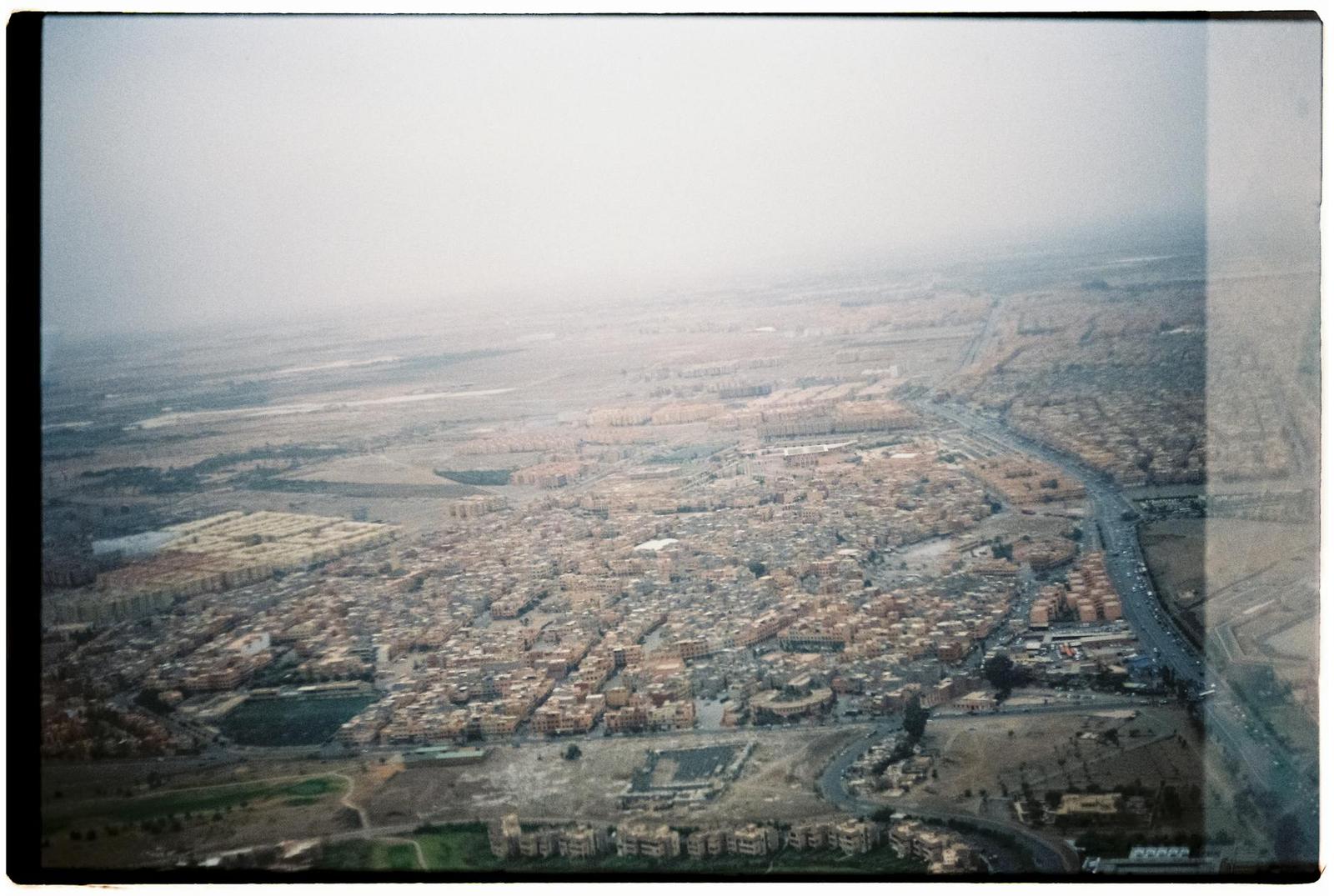 Grainy aerial photograph of a dense sandy-toned city spreading across flat terrain