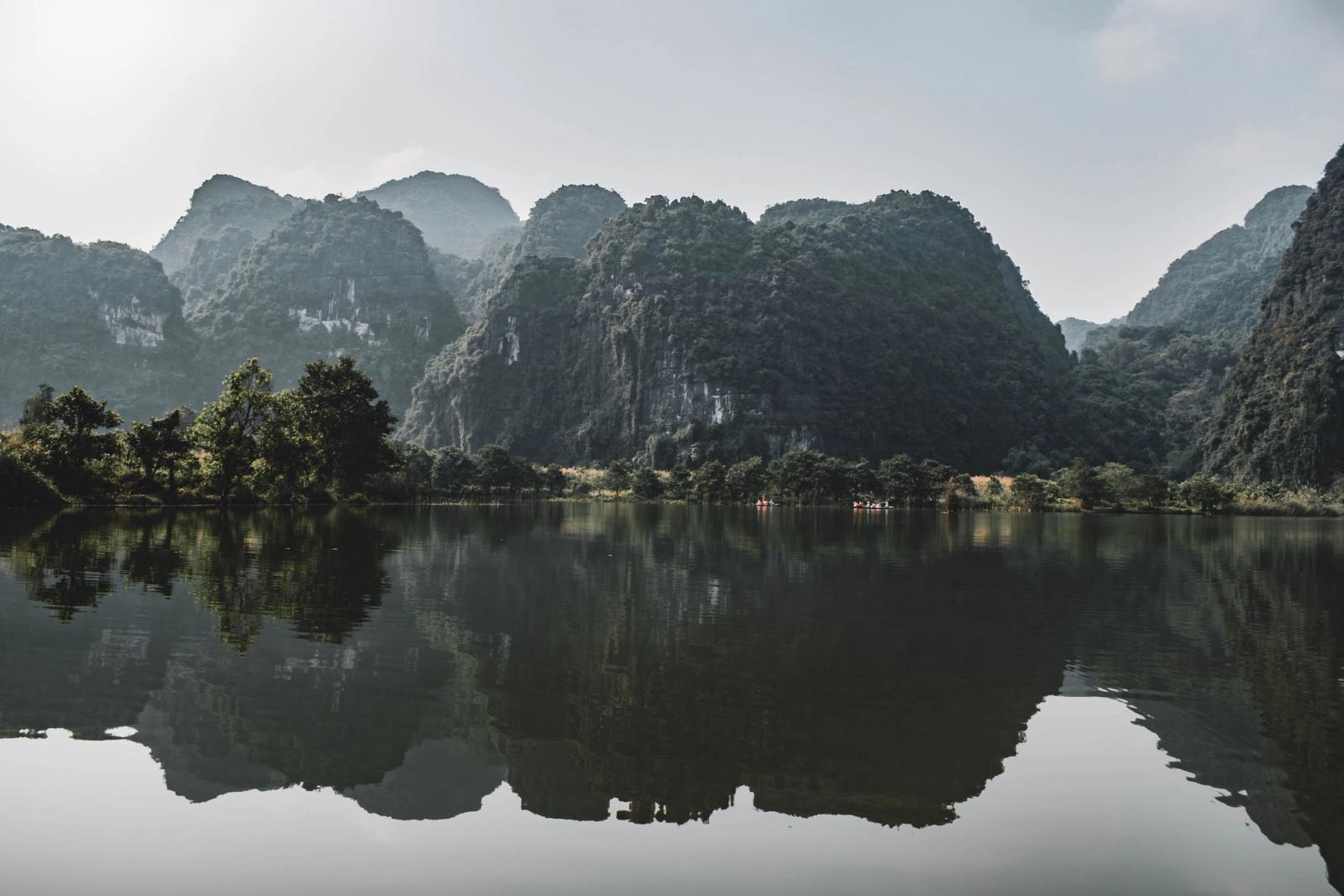 Peaceful reflection of limestone mountains in Ninh Bình, Vietnam's tranquil waters