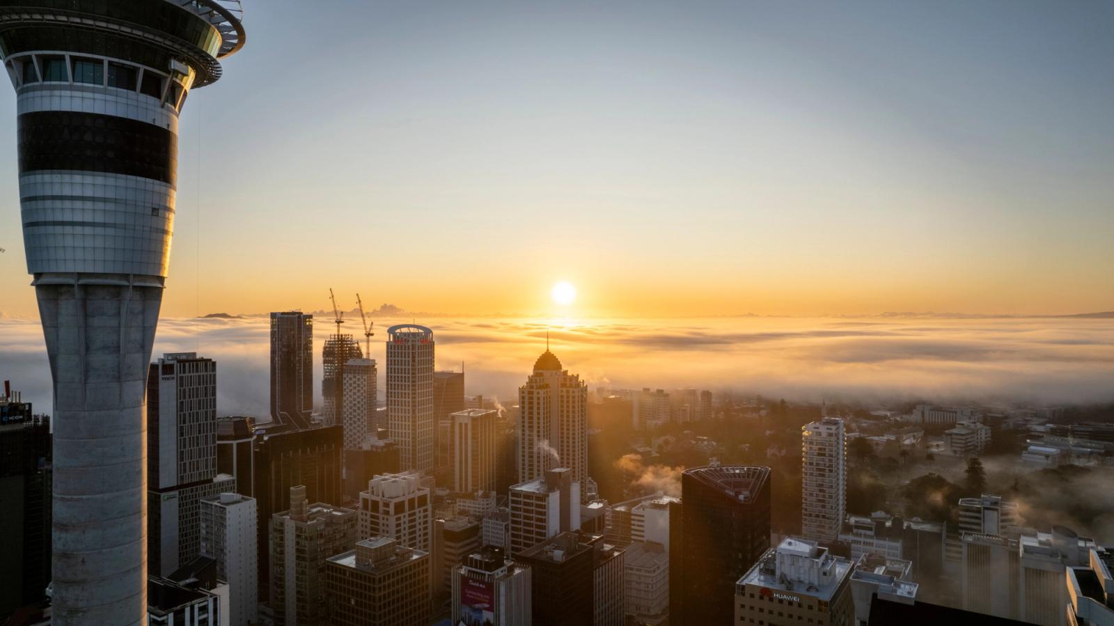 A stunning view of Auckland's skyline with the Sky Tower at sunrise, enveloped in morning fog