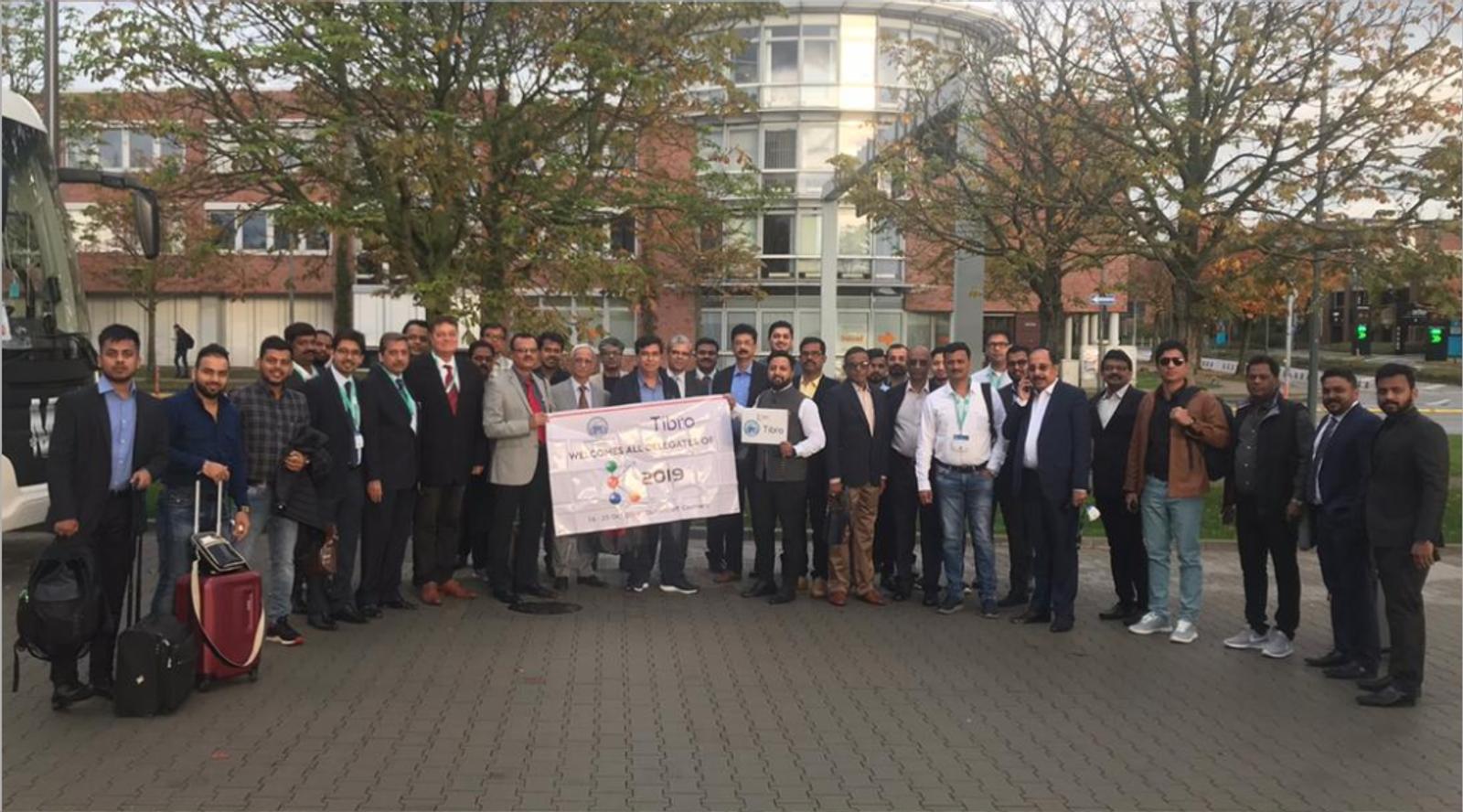 A large group of professionals posing outdoors with a banner.
