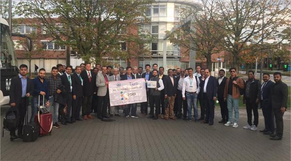 A large group of professionals posing outdoors with a banner.