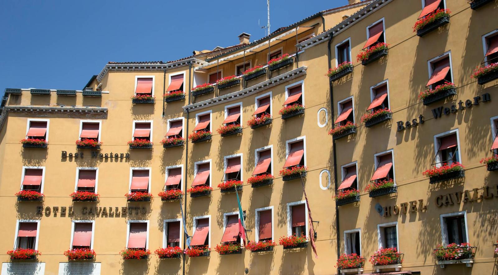 A row of hotel windows with red awnings and flower boxes along the facade