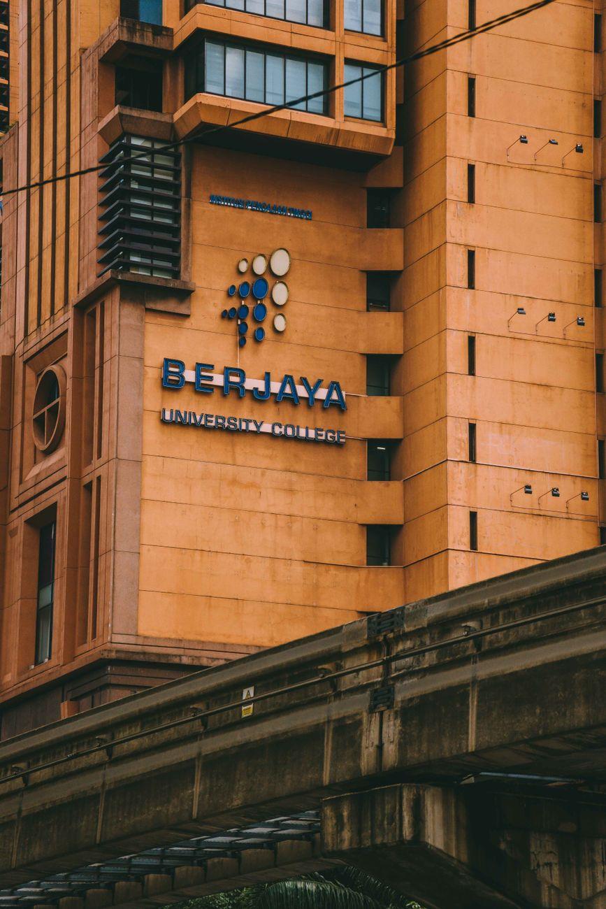 Close-up of a university building facade with signage beside an elevated rail line