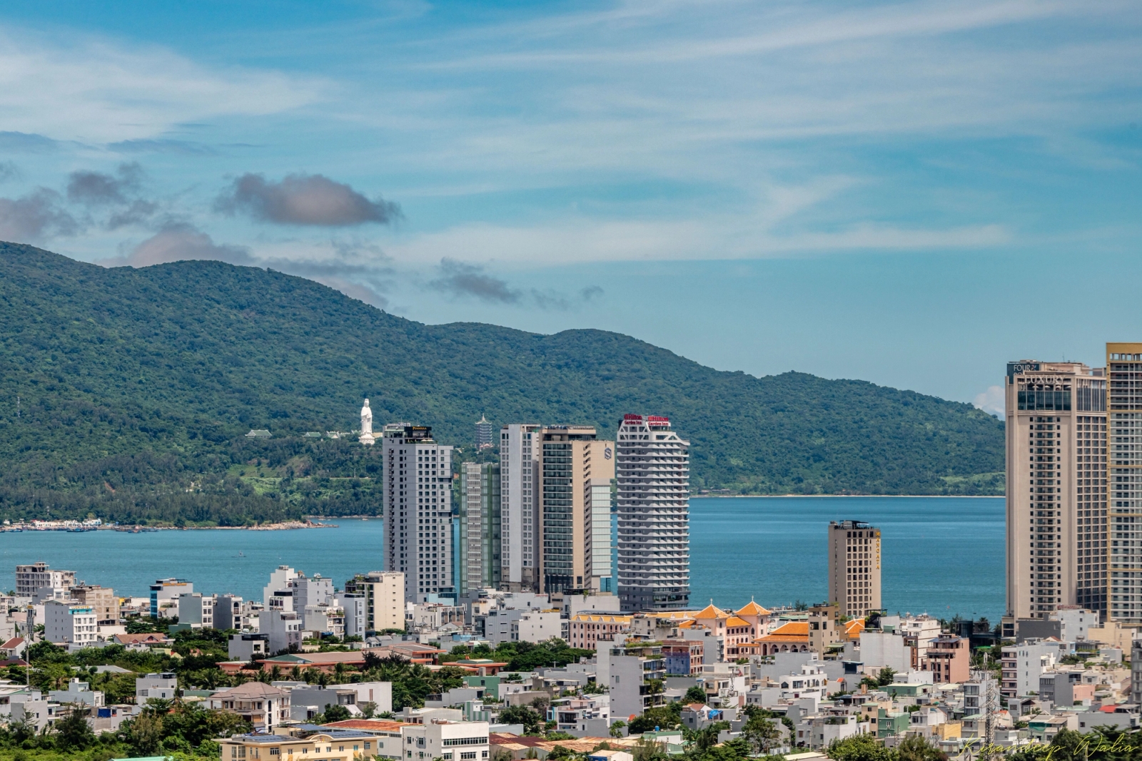 Cityscape of Da Nang, Vietnam with buildings, ocean, and lush mountains