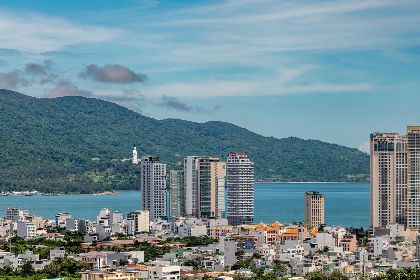 Cityscape of Da Nang, Vietnam with buildings, ocean, and lush mountains