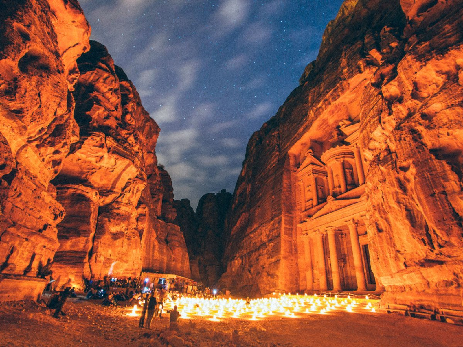 A rock-carved treasury facade lit at night with candles lining the canyon floor