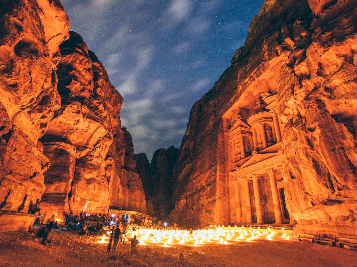 A rock-carved treasury facade lit at night with candles lining the canyon floor