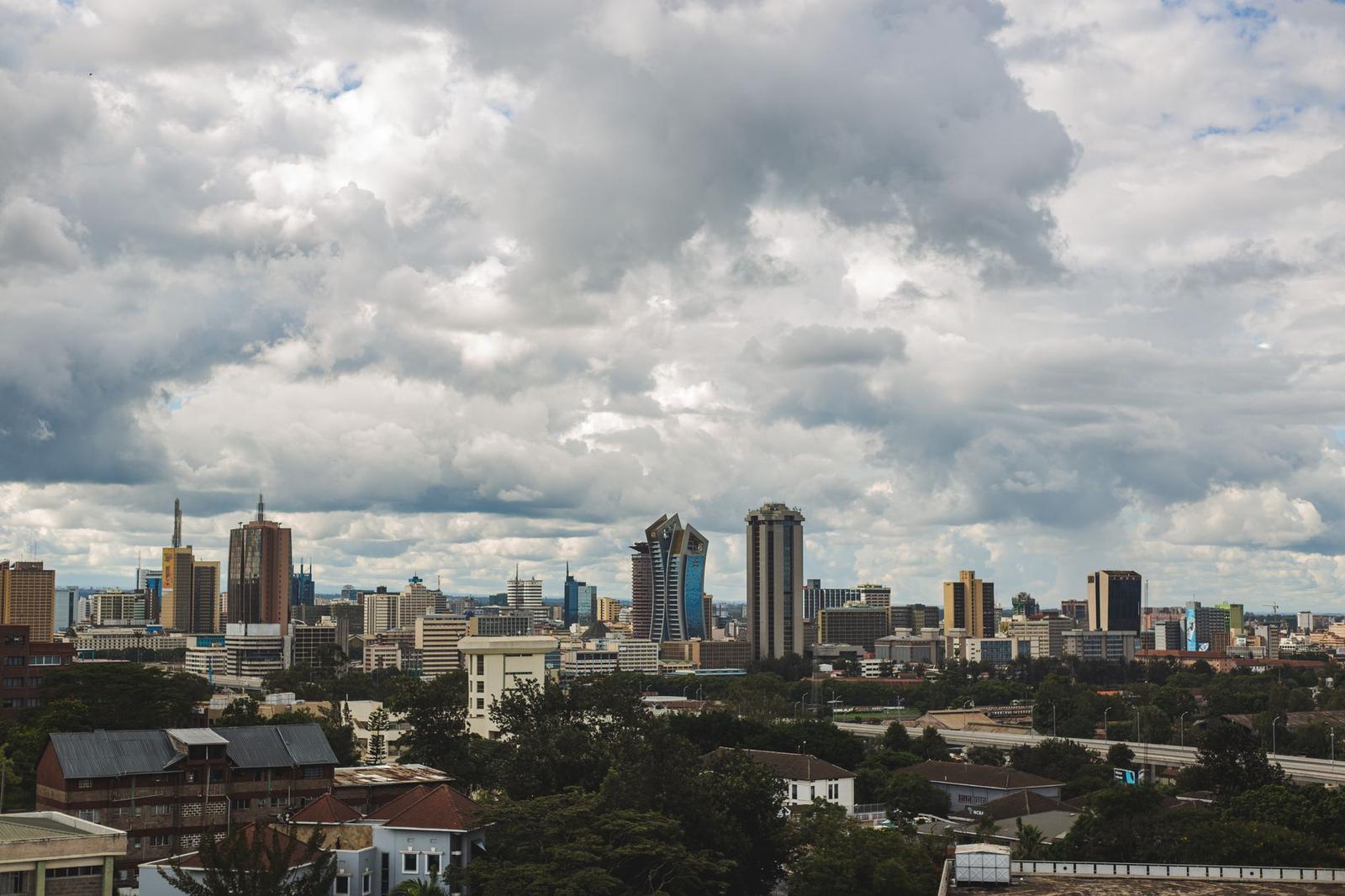 A city skyline of mixed high-rises under a heavy cloudy sky