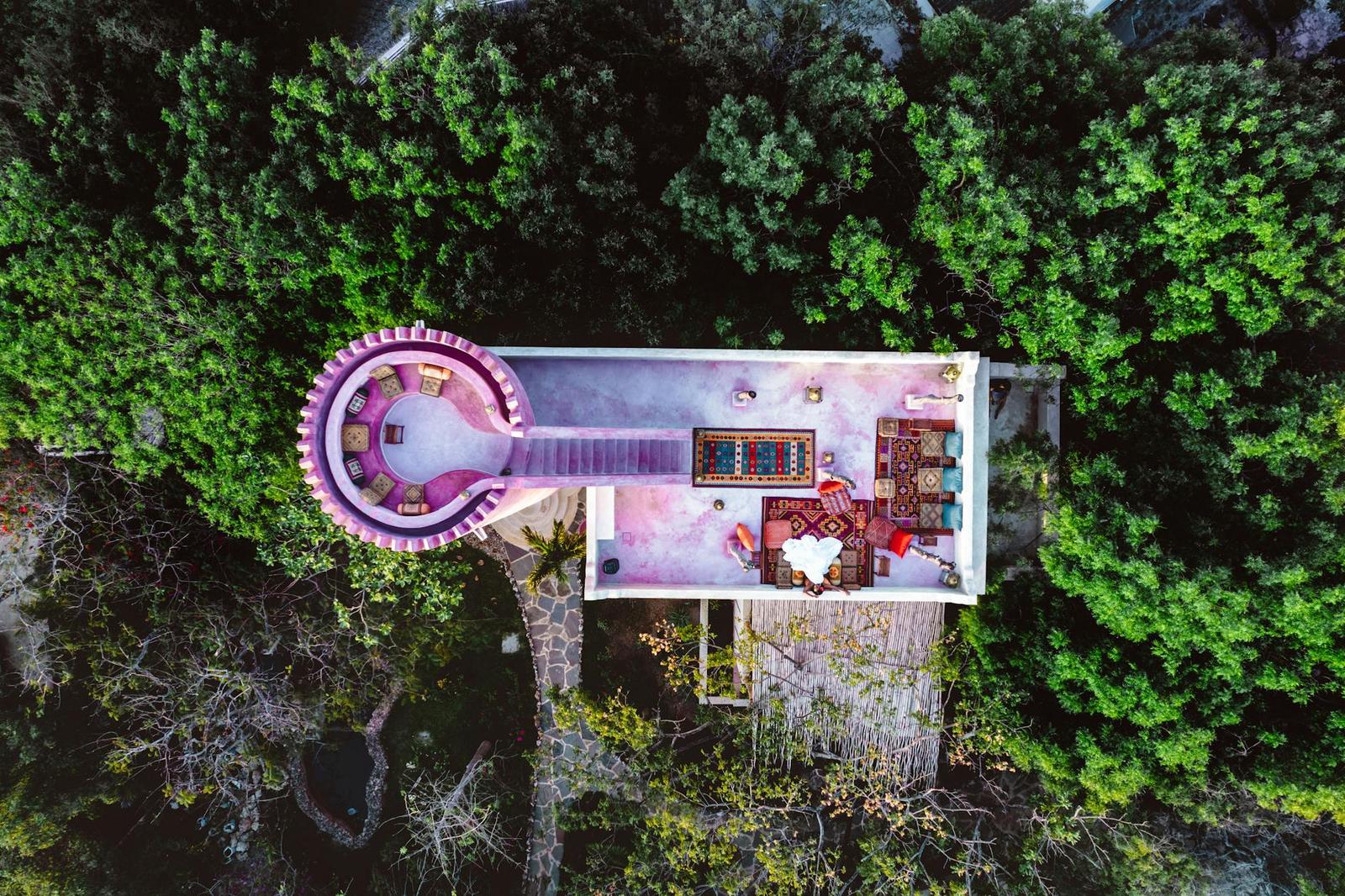 An aerial view of a circular thatched pavilion surrounded by dense forest canopy