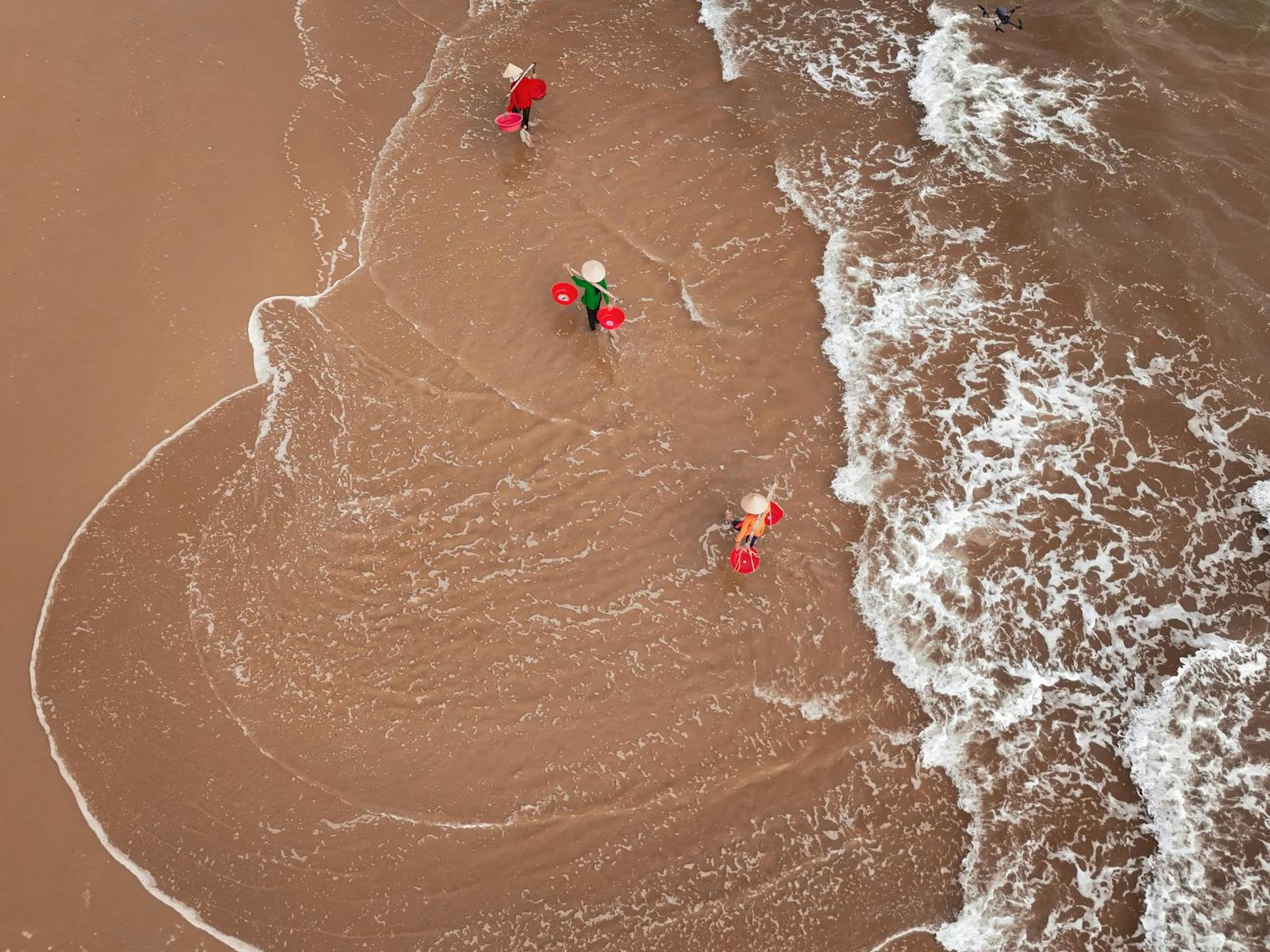 Aerial view of figures wading through breaking waves on a muddy beach