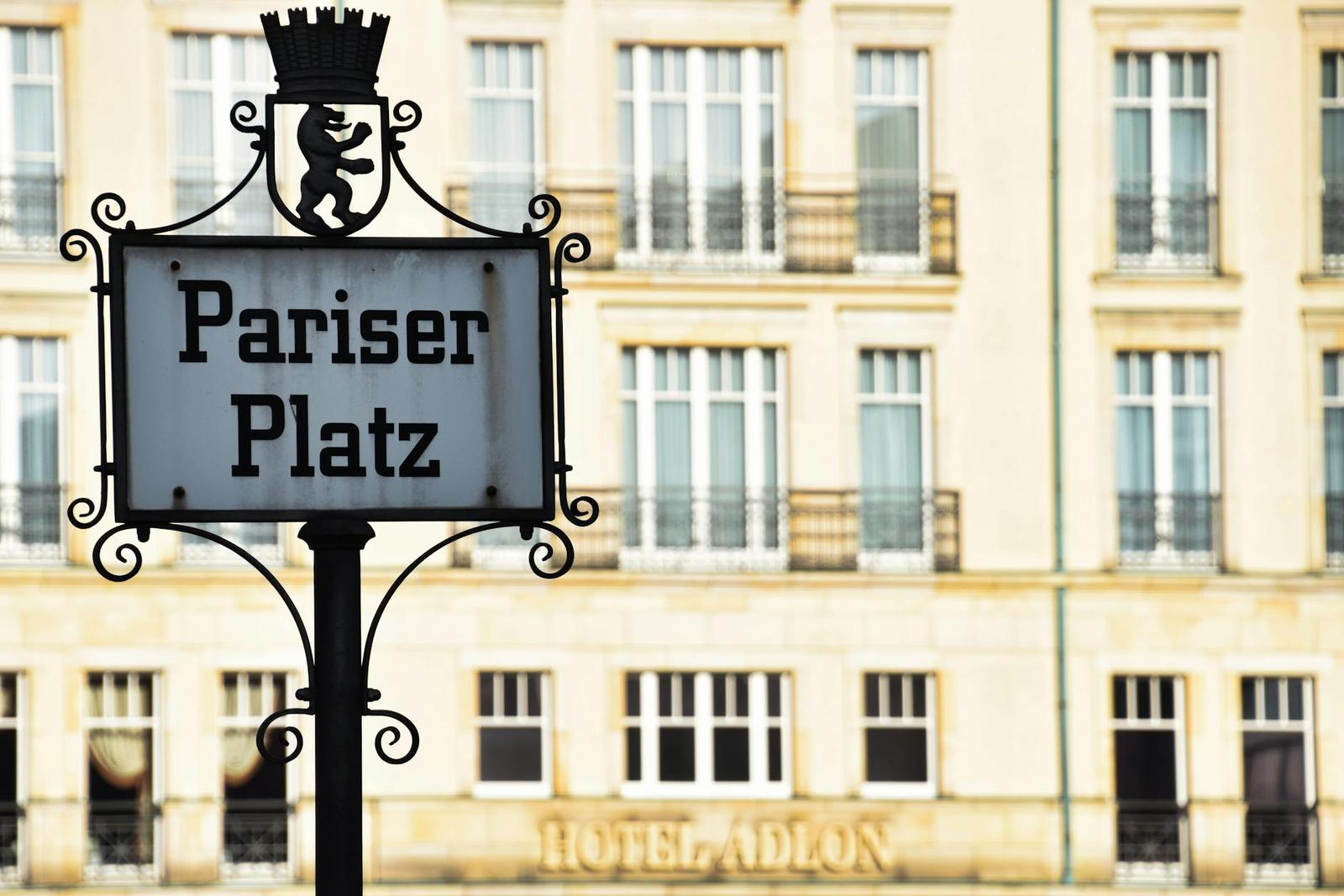 An ornate street sign in front of a grand stone hotel facade with rows of windows
