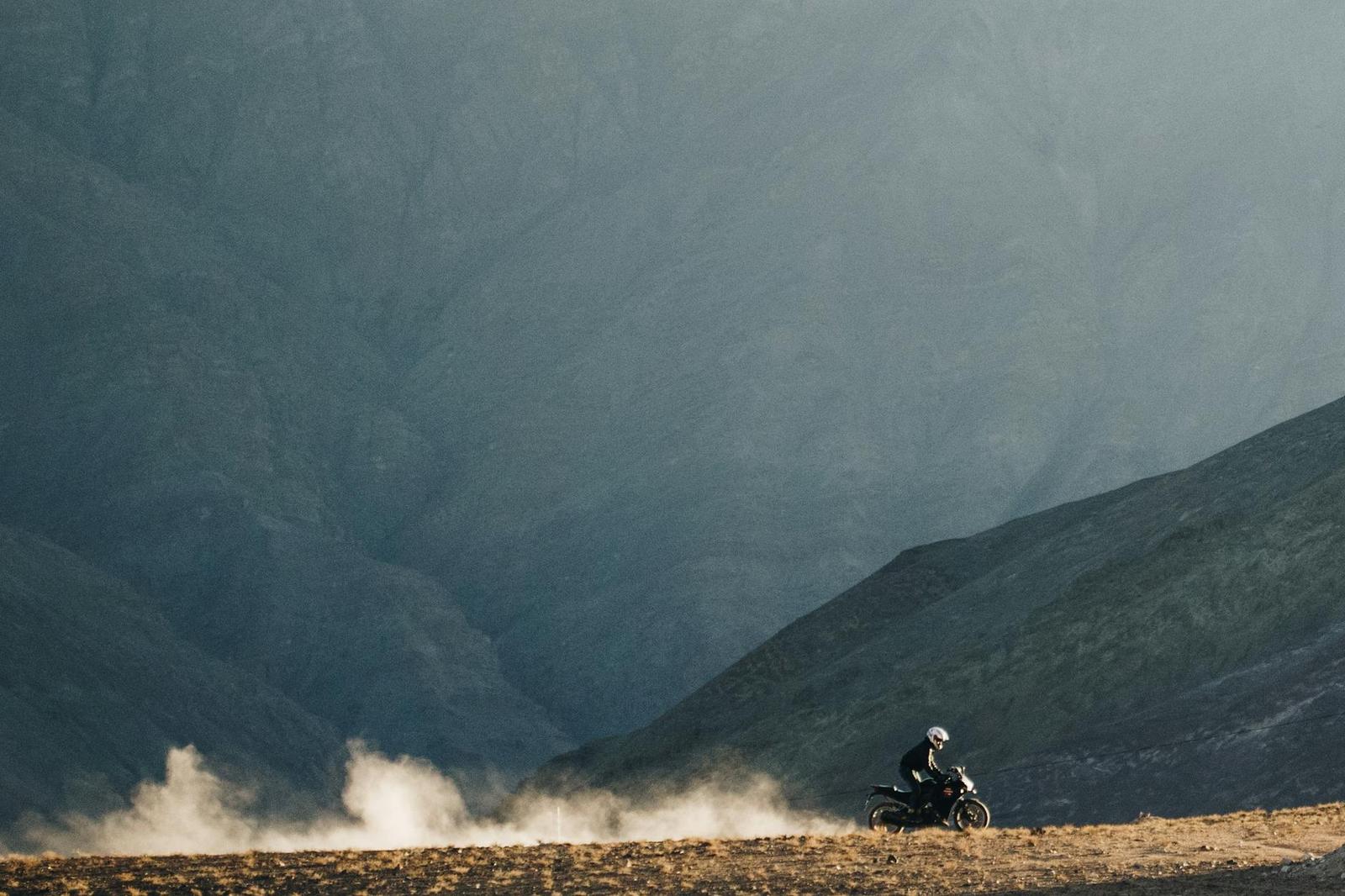 A motorcyclist kicking up dust on a misty mountain track