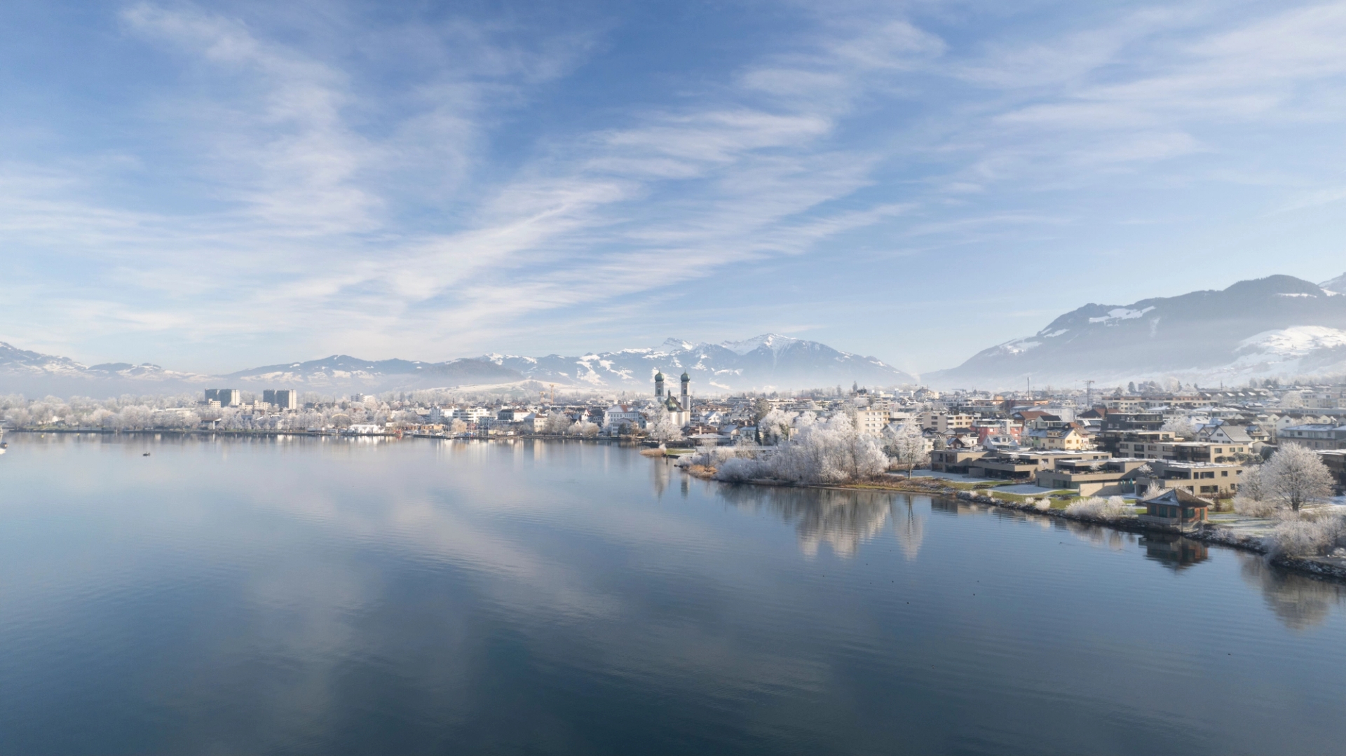 A serene winter view of Altendorf with mountains and reflection on the lake