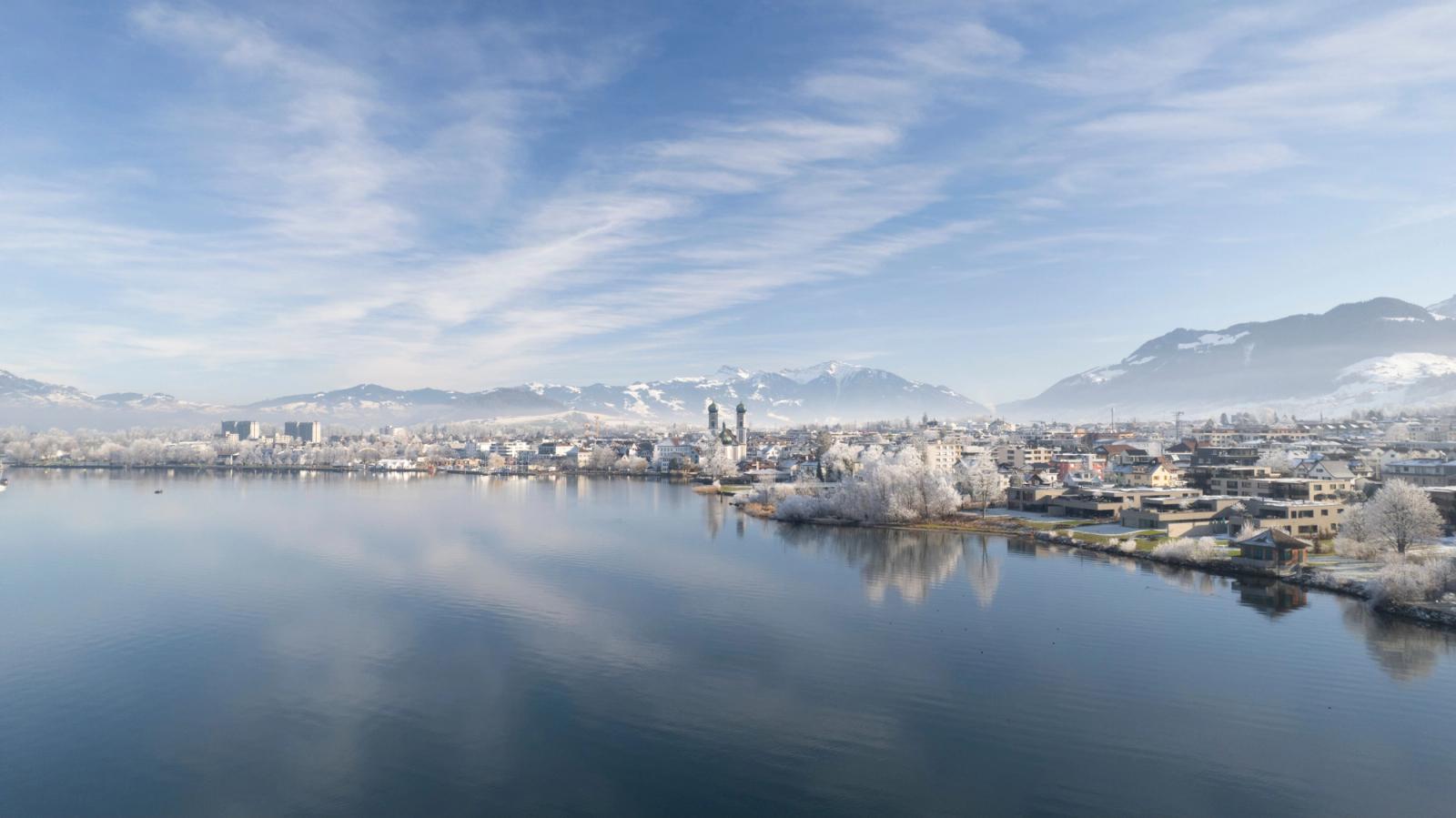 A serene winter view of Altendorf with mountains and reflection on the lake