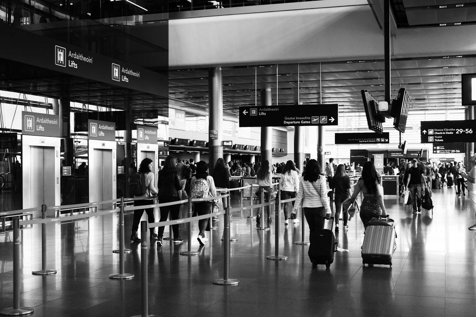 Black and white view of travellers queuing with luggage at an airport check-in