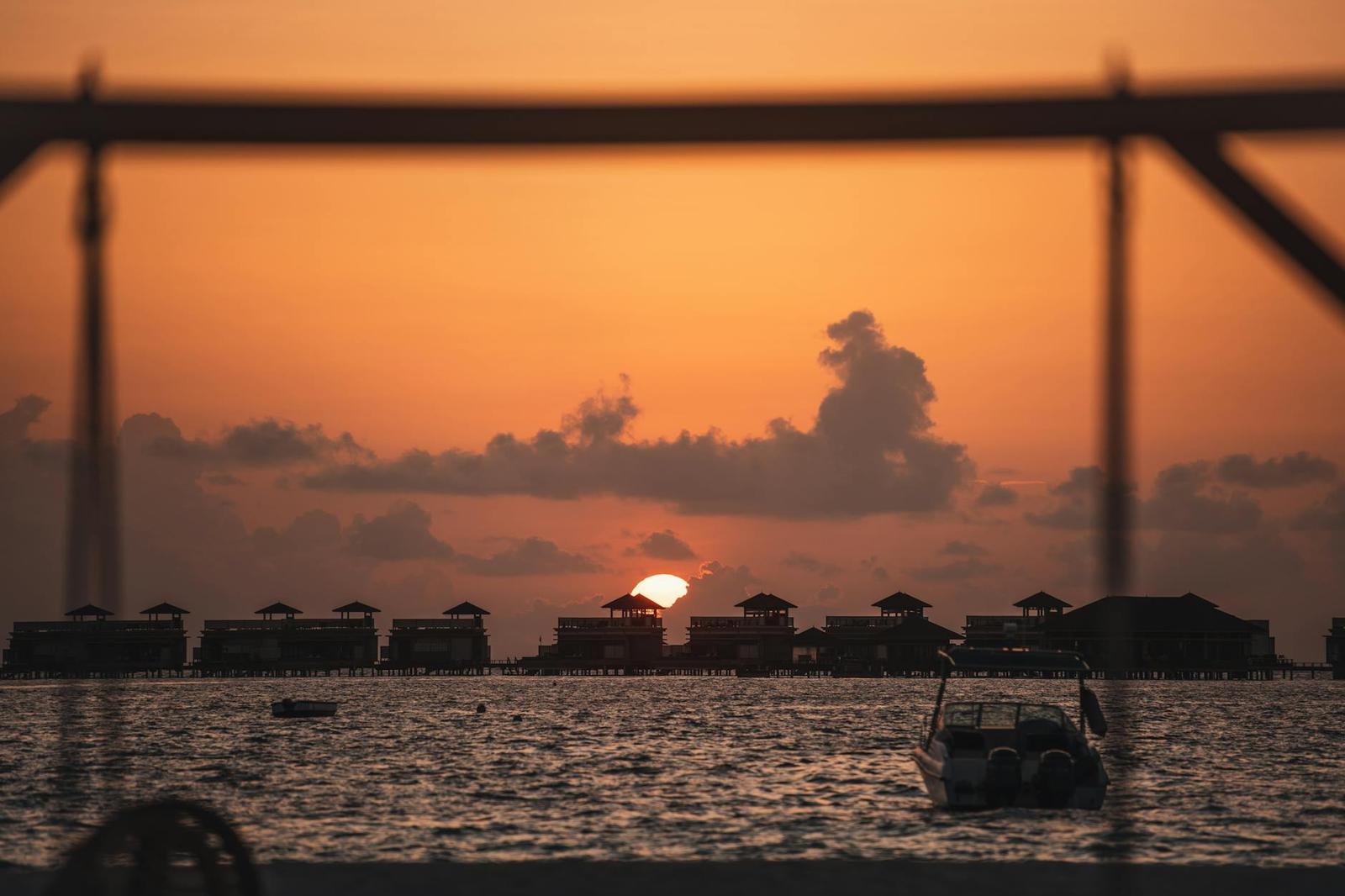 Silhouetted overwater bungalows and a moored boat at sunset