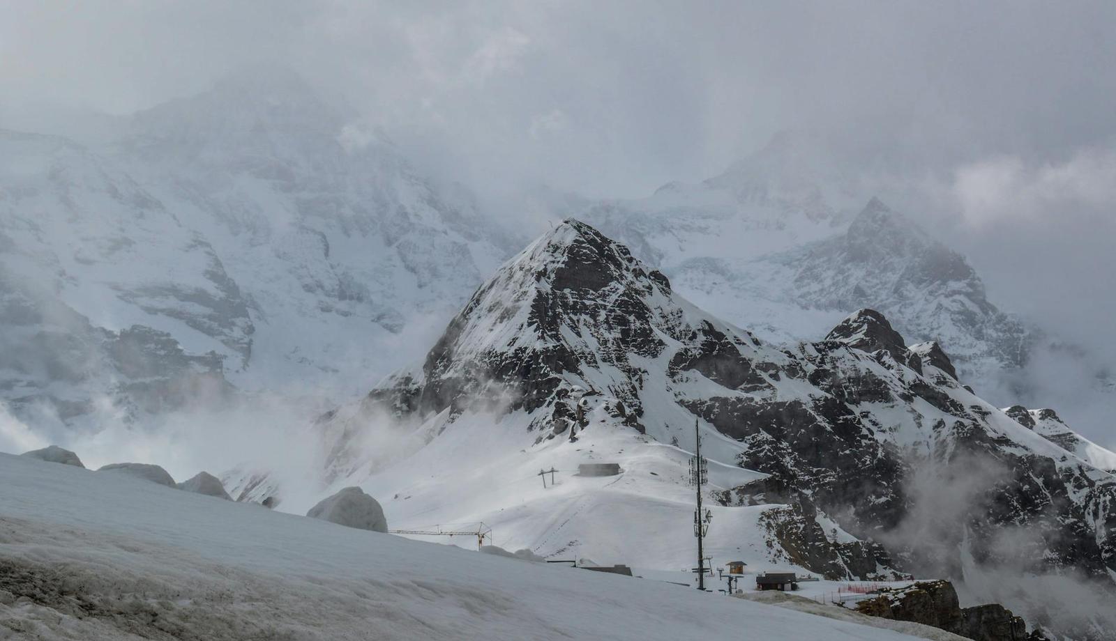 Cable car station dwarfed by a jagged snow-covered peak in mist