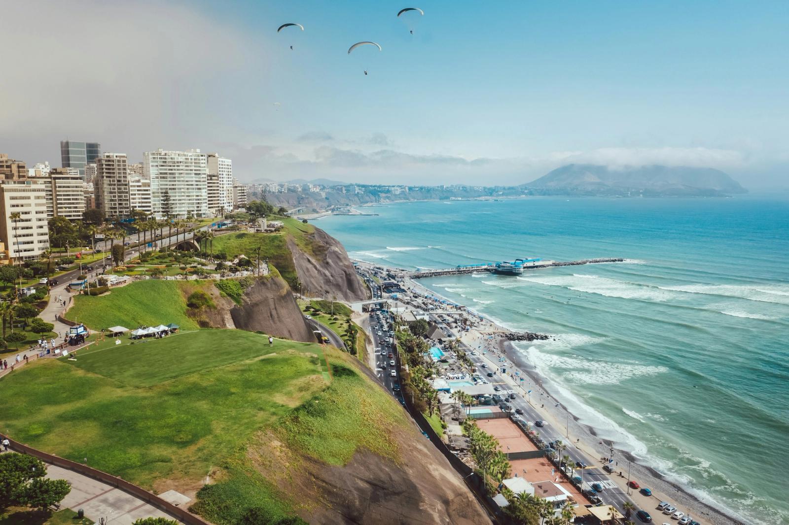 Paragliders over a clifftop park above a curving coastal boardwalk