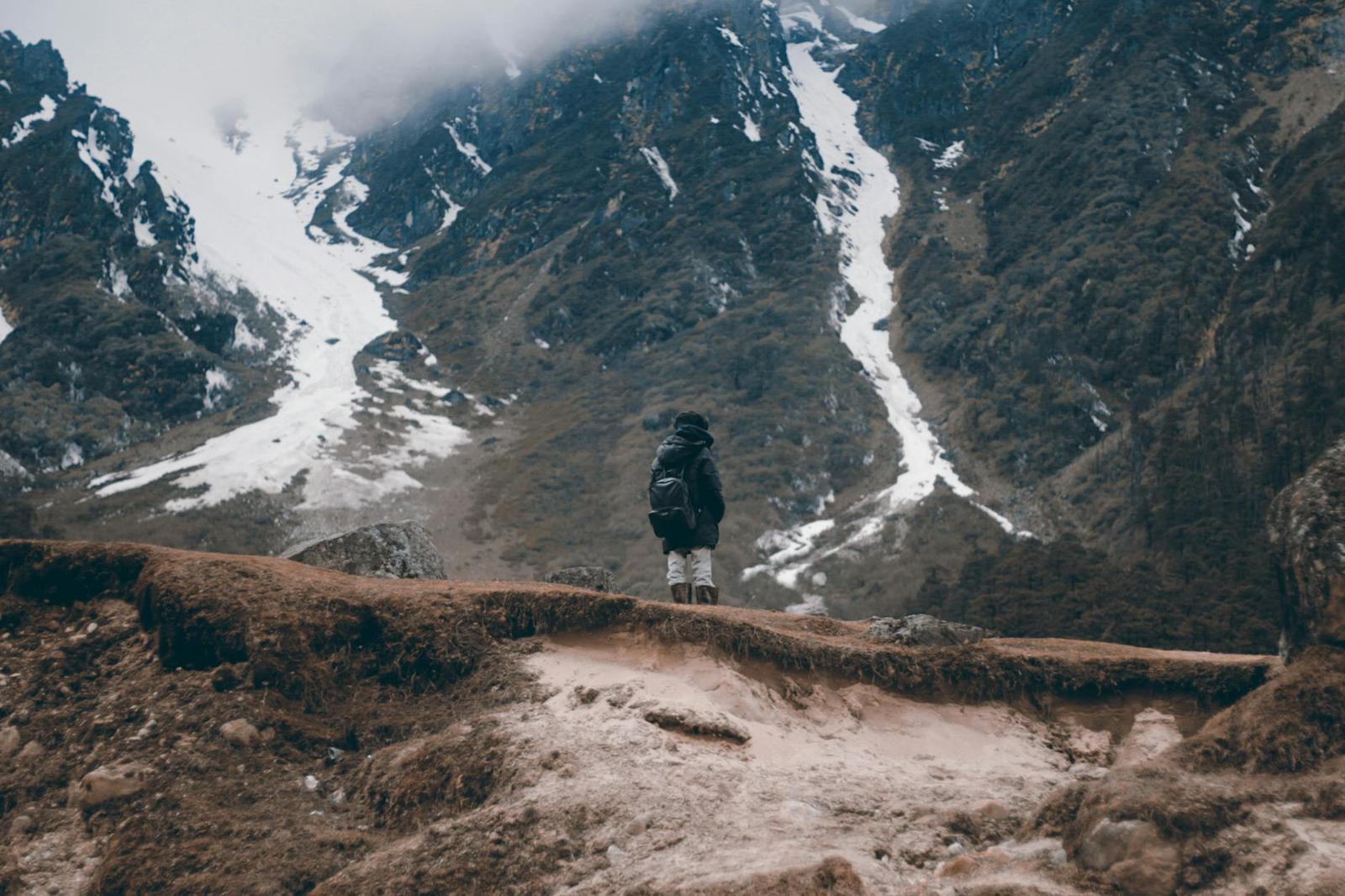 A hiker standing on a ridge overlooking snow-streaked mountain slopes