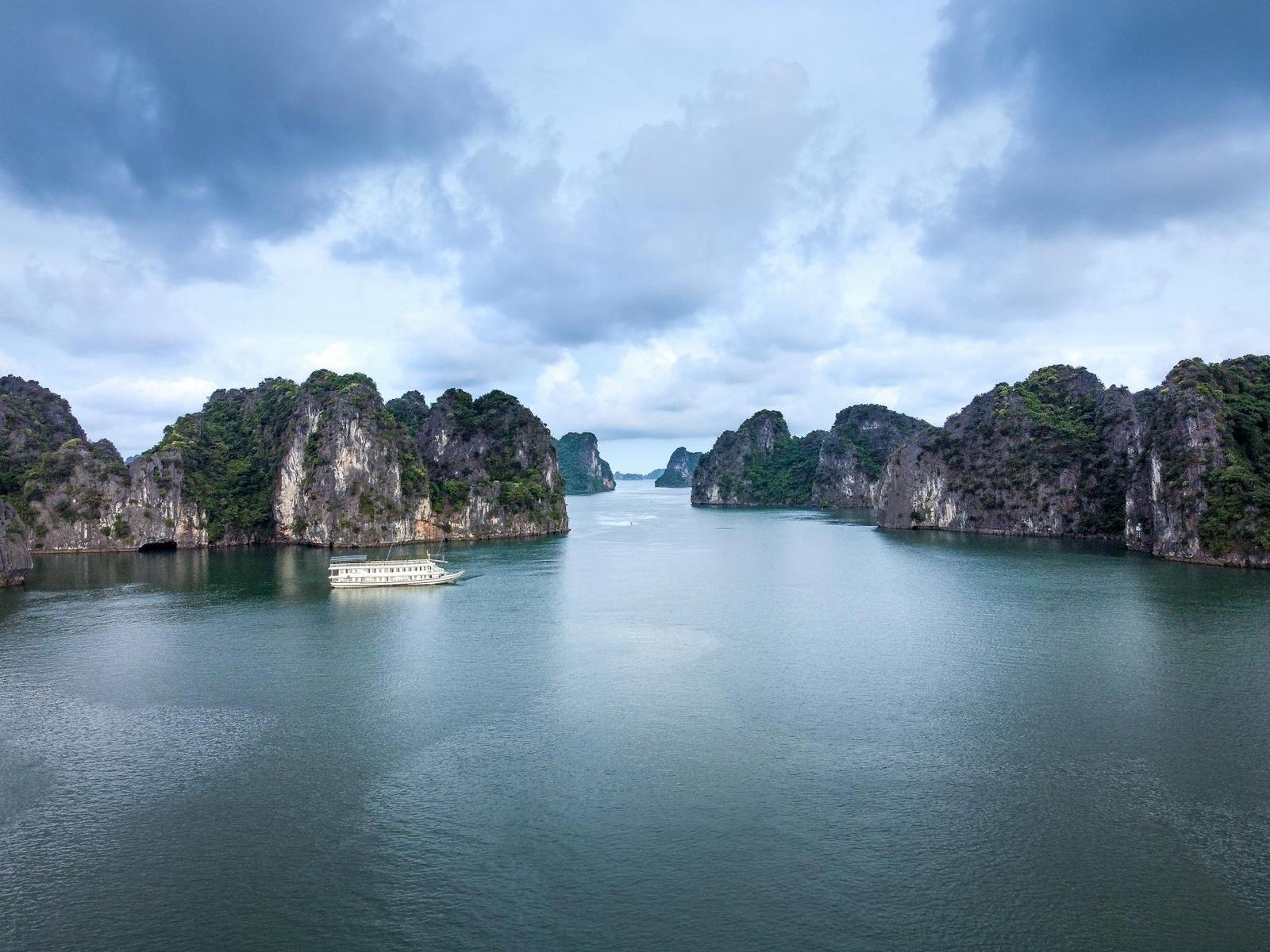 A breathtaking aerial view of limestone islands and a ship in Halong Bay, Vietnam under a cloudy sky