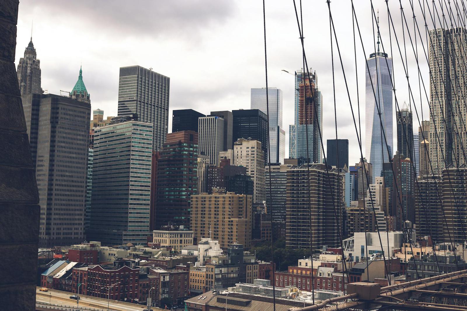 A dense high-rise skyline seen through suspension bridge cables under an overcast sky