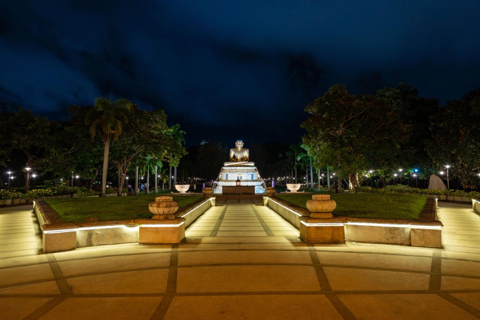 A serene nighttime view of an illuminated Buddha statue surrounded by lush greenery in Colombo, Sri Lanka